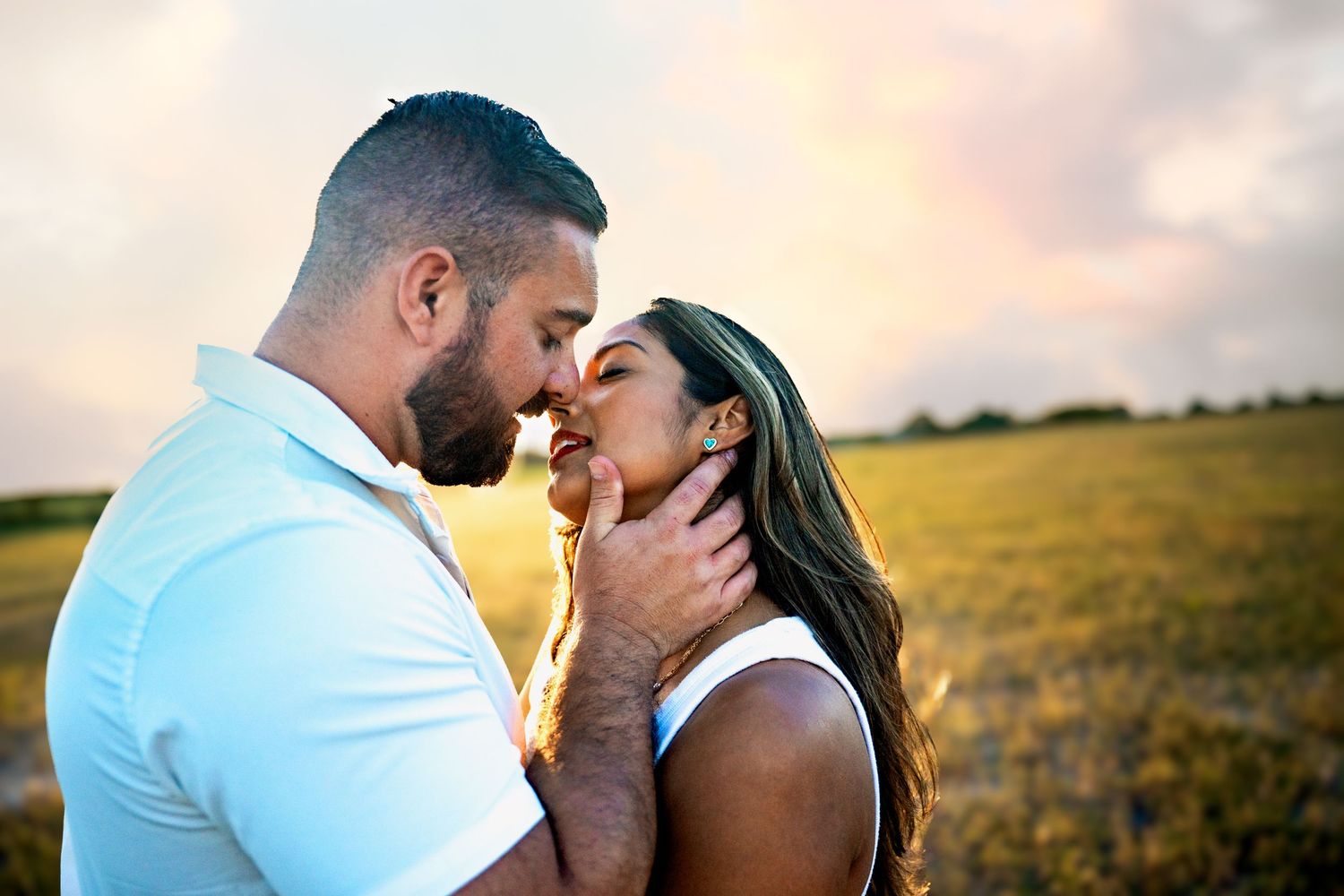 Romantic couple sharing a tender moment in a golden sunset field, man gently holding womans face.