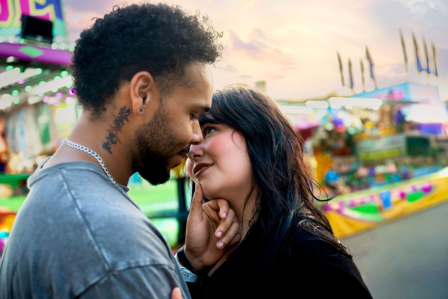 Romantic couple sharing an intimate moment at a colorful amusement park at sunset.