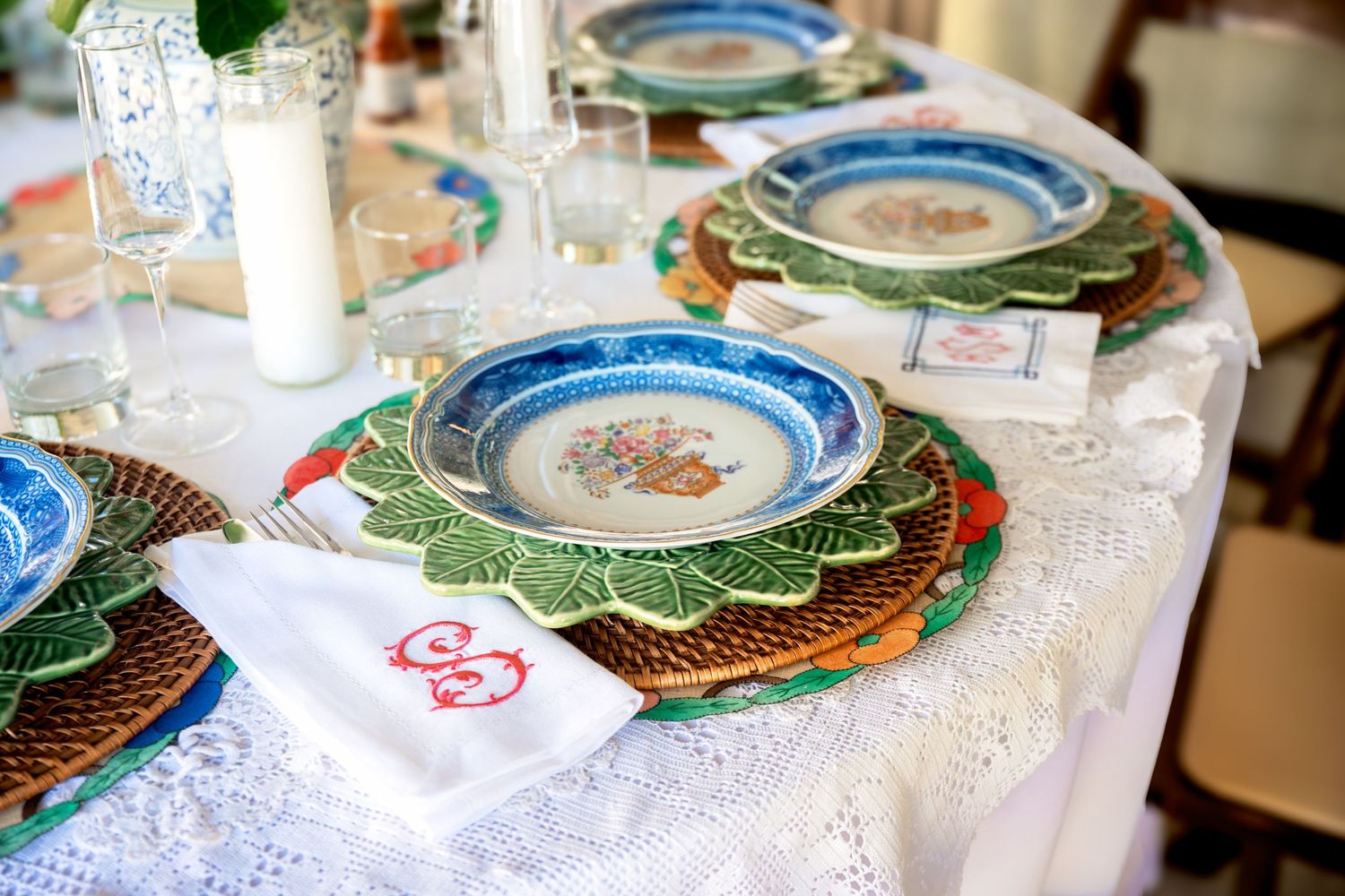 Elegant table setting with layered decorative plates, lace tablecloth, monogrammed napkin, and crystal glasses for a formal dining occasion.