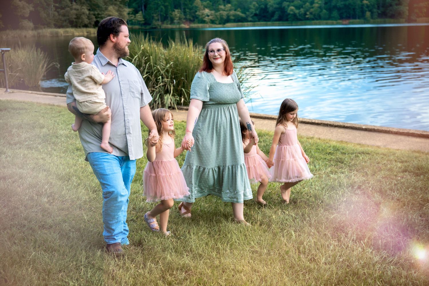 Family of five walks hand in hand by a lake in coordinated outfits.