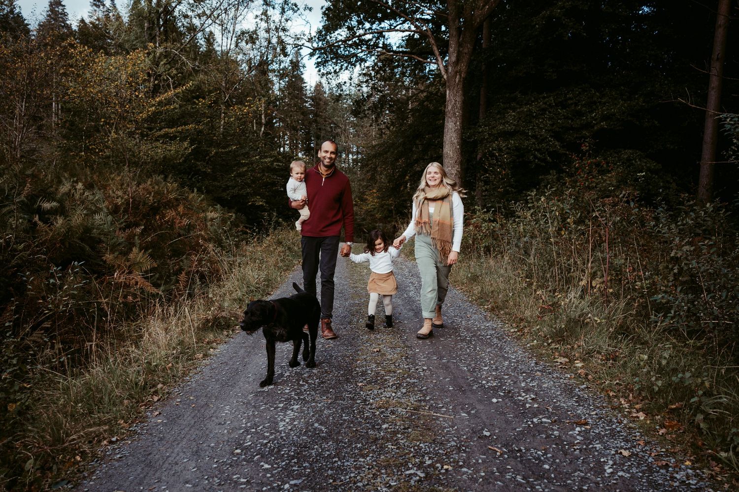 People walking through a wooded trail in autumn with evergreen trees and fallen leaves along the path.