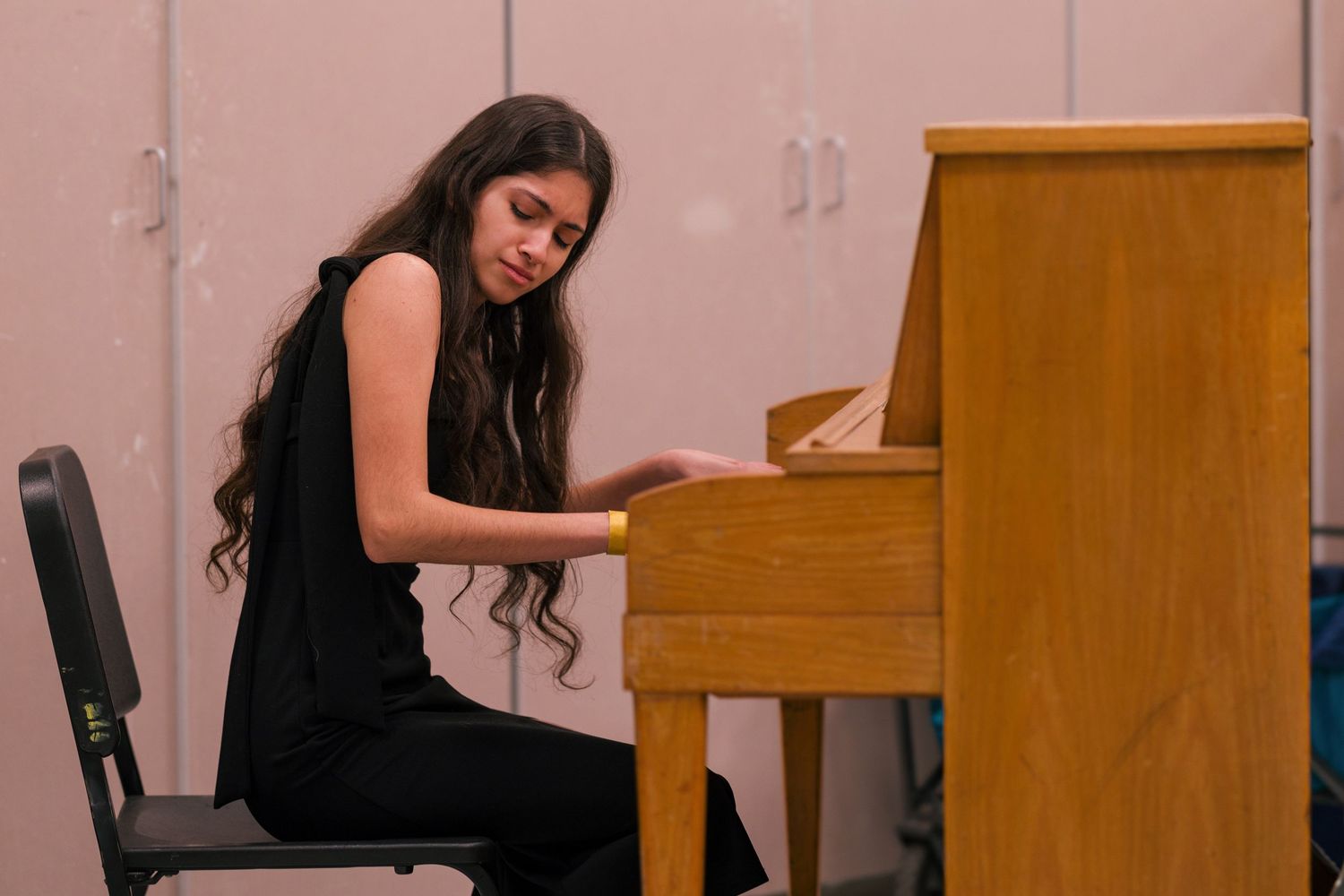 A person wearing black clothing sits at a wooden piano ready to perform.