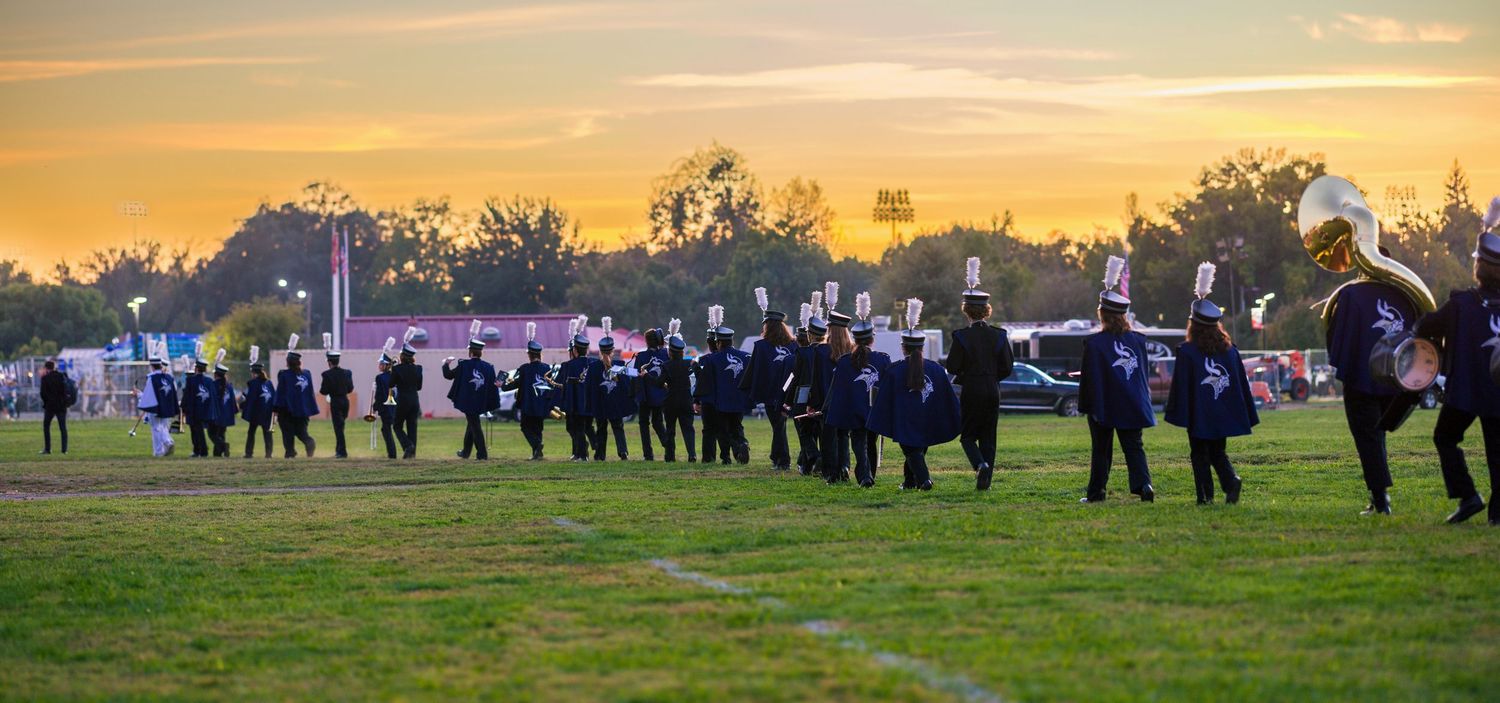 A panoramic view of a rural field at sunset with silhouettes of trees and figures gathered in the distance.