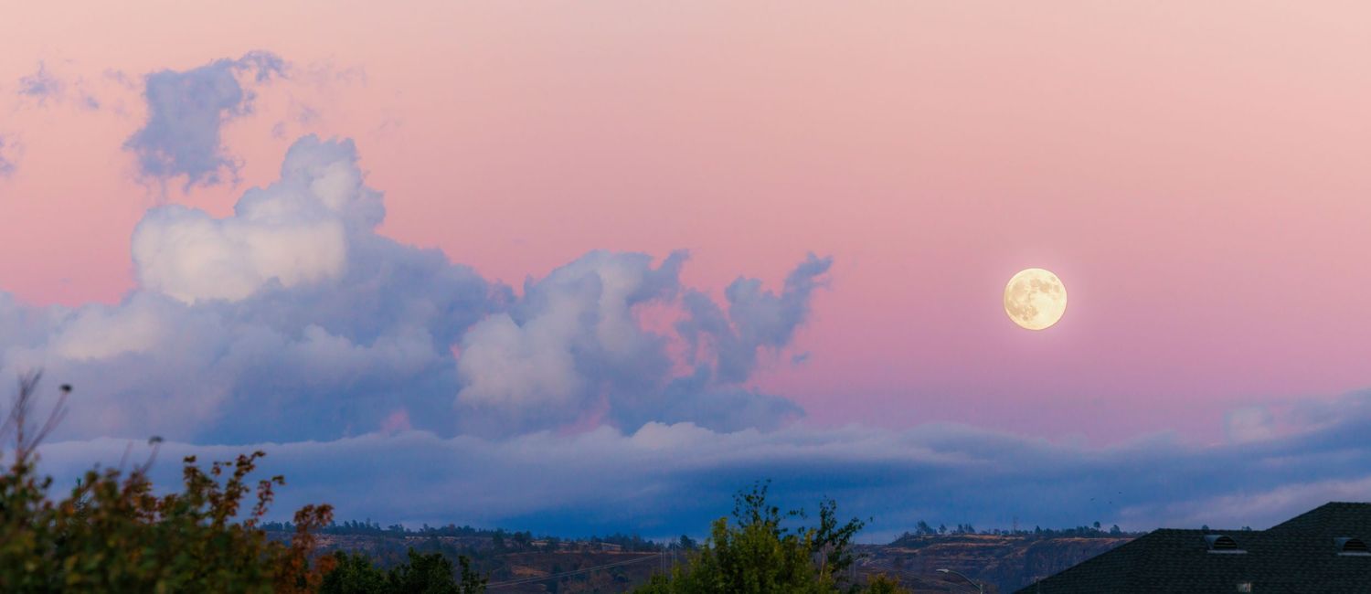 A panoramic view of a pink and purple sunset sky with clouds reflecting over a tranquil landscape.