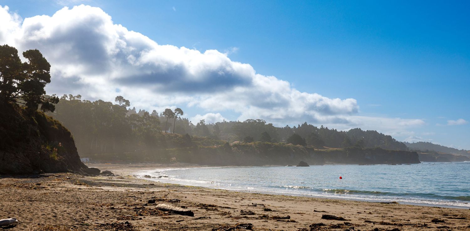 Panoramic view of a sandy beach coastline with ocean waves and cliffs under blue sky.