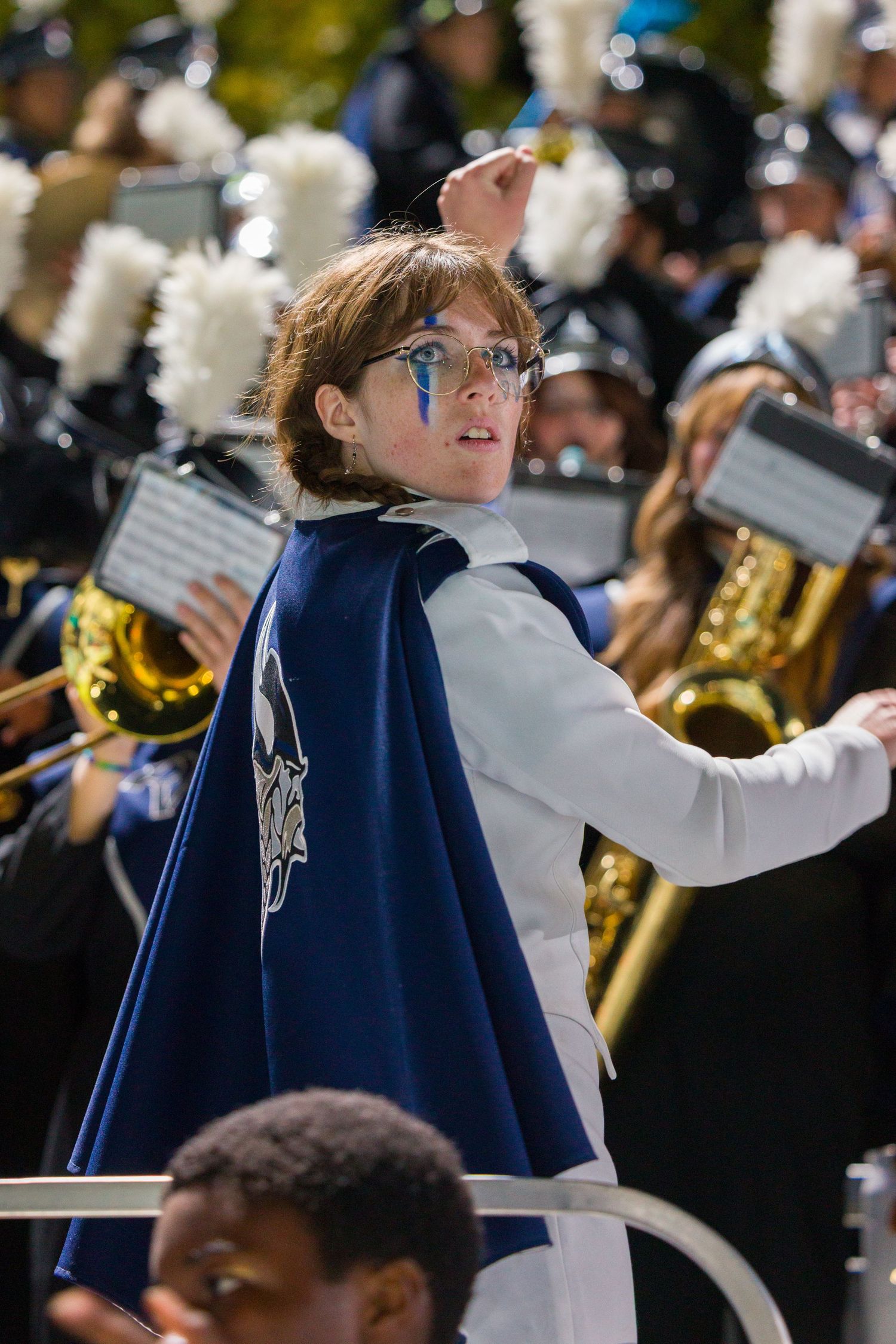Marching band performers in navy blue uniforms holding sheet music during an outdoor performance.