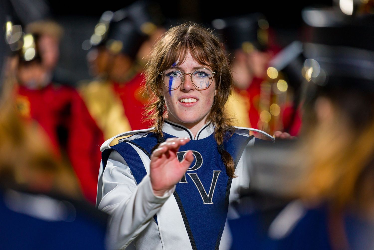 A marching band performer in a blue and white uniform plays an instrument during a performance.