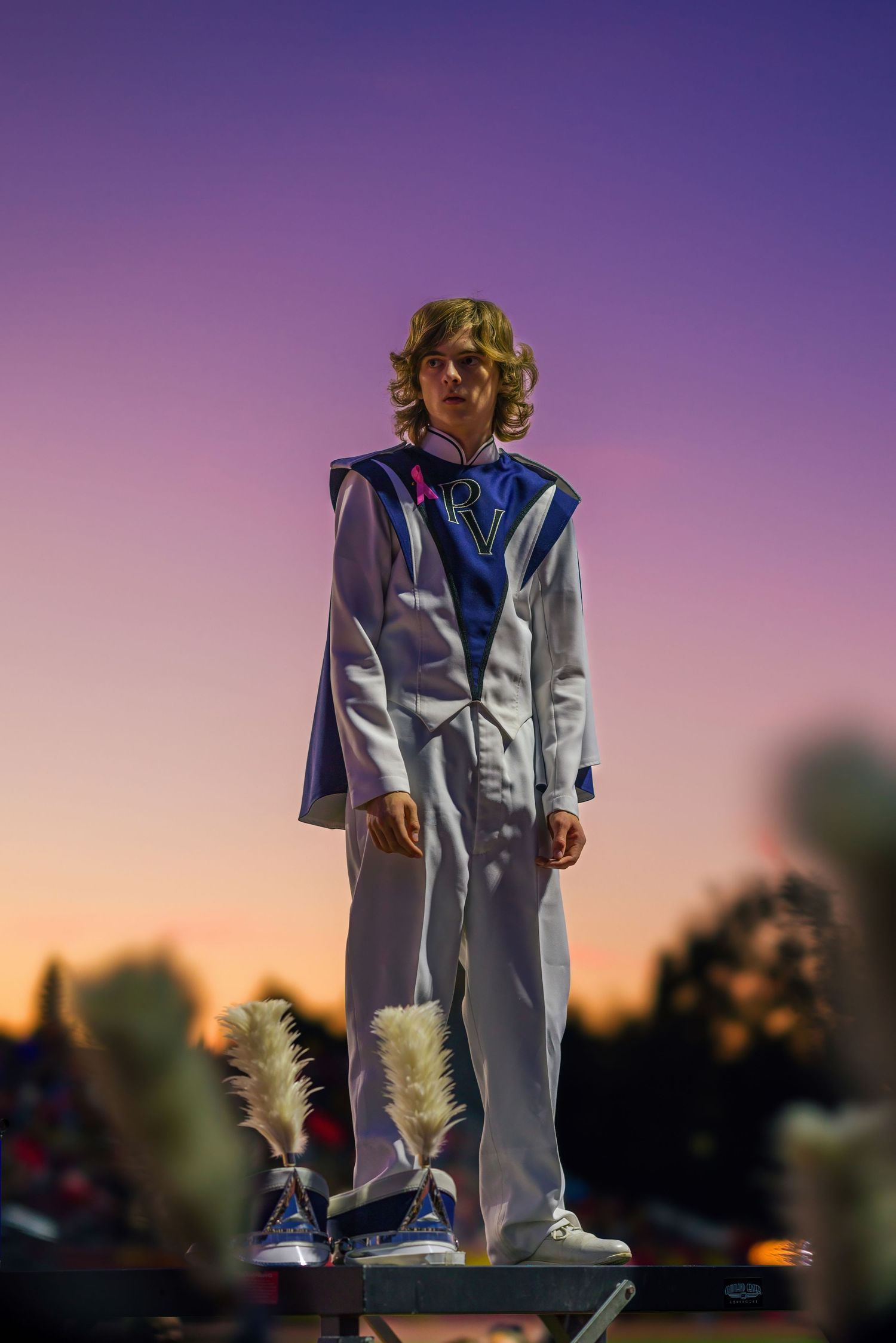 Figure in white jumpsuit strikes a dramatic pose against purple sunset sky during outdoor photo shoot.
