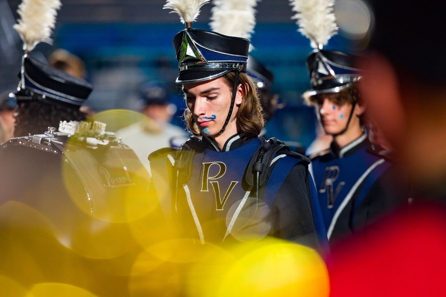 Marching band members in blue uniforms perform during a halftime show at a football stadium.