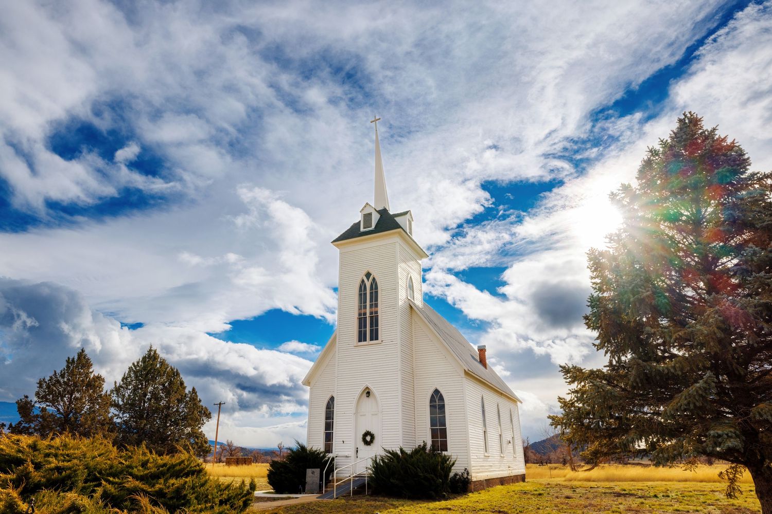 Historic white church steeple rises against dramatic blue and white cloudy sky in autumn countryside setting.