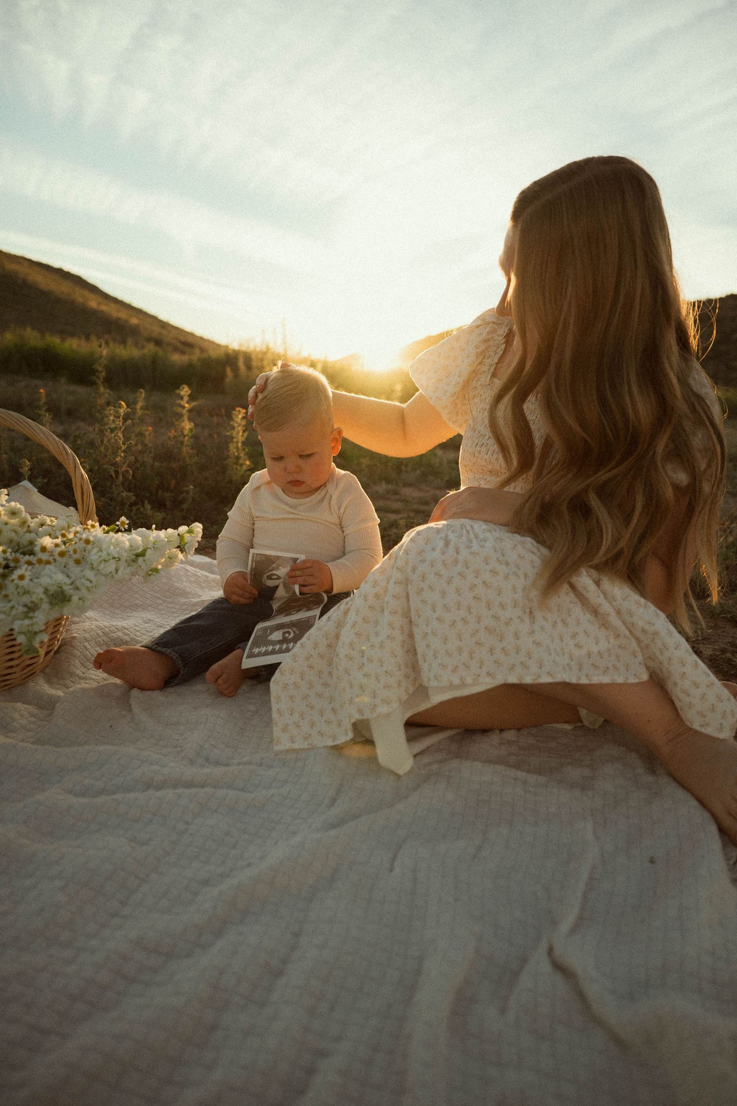 Family relaxing on a blanket during golden hour sunset in a scenic mountain landscape.
