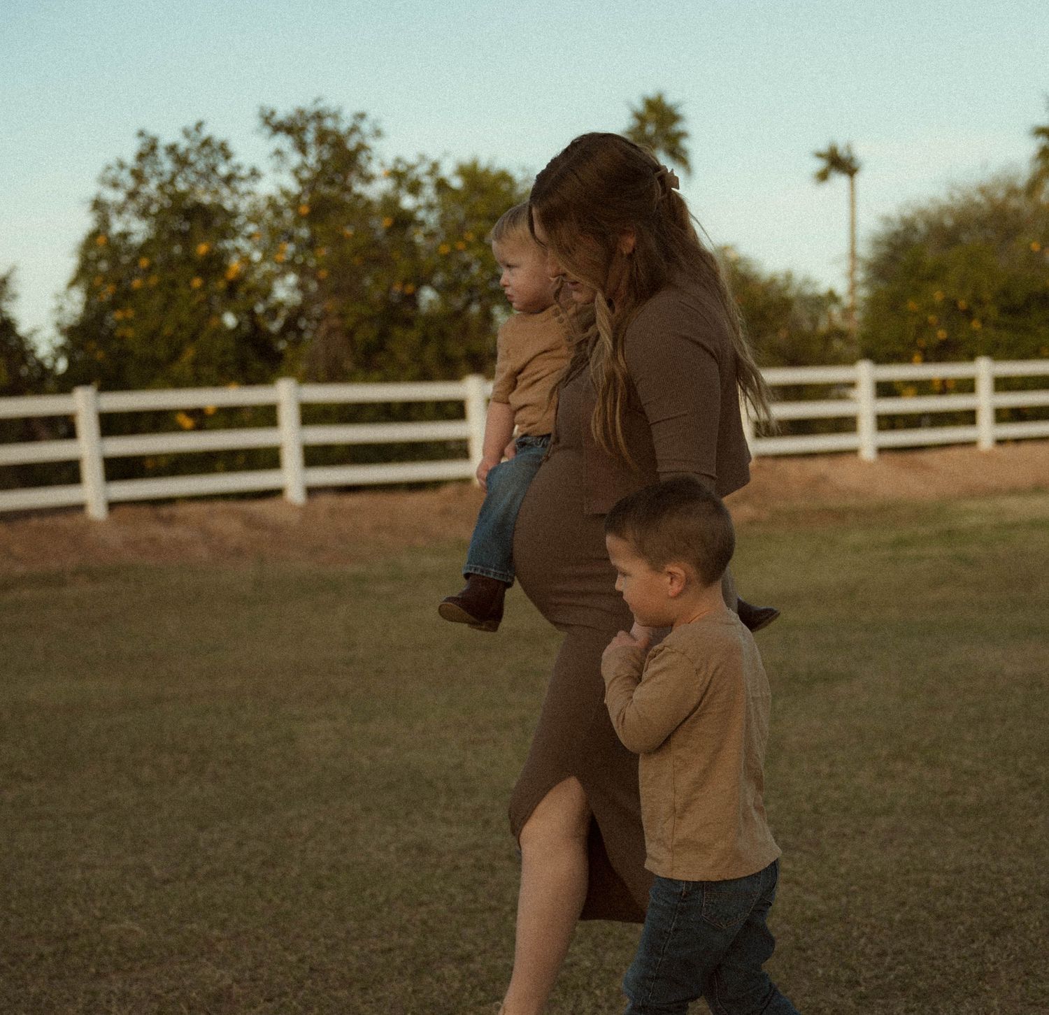pregnant mom and her sons walks across a pasture during their phoenix family photos