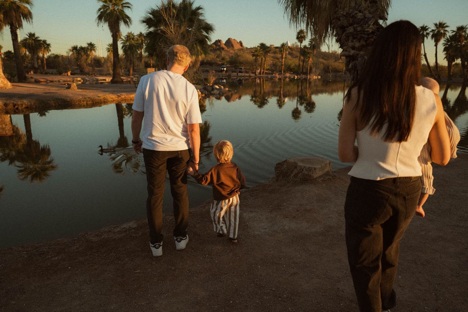 Family enjoying a peaceful sunset by a reflective lake with palm trees at golden hour.