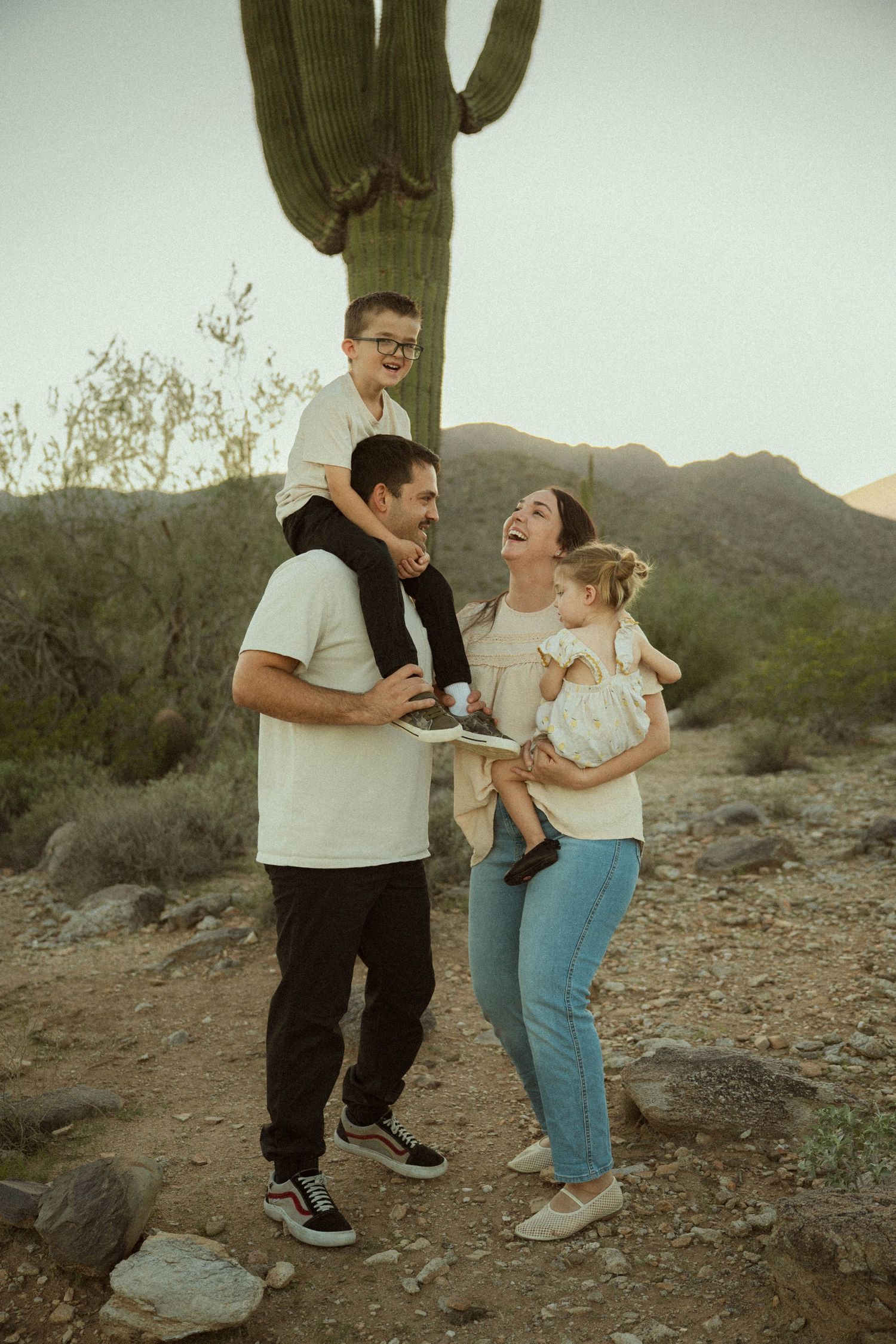 A family shares a joyful moment together in front of a tall saguaro cactus in the Arizona desert at sunset.