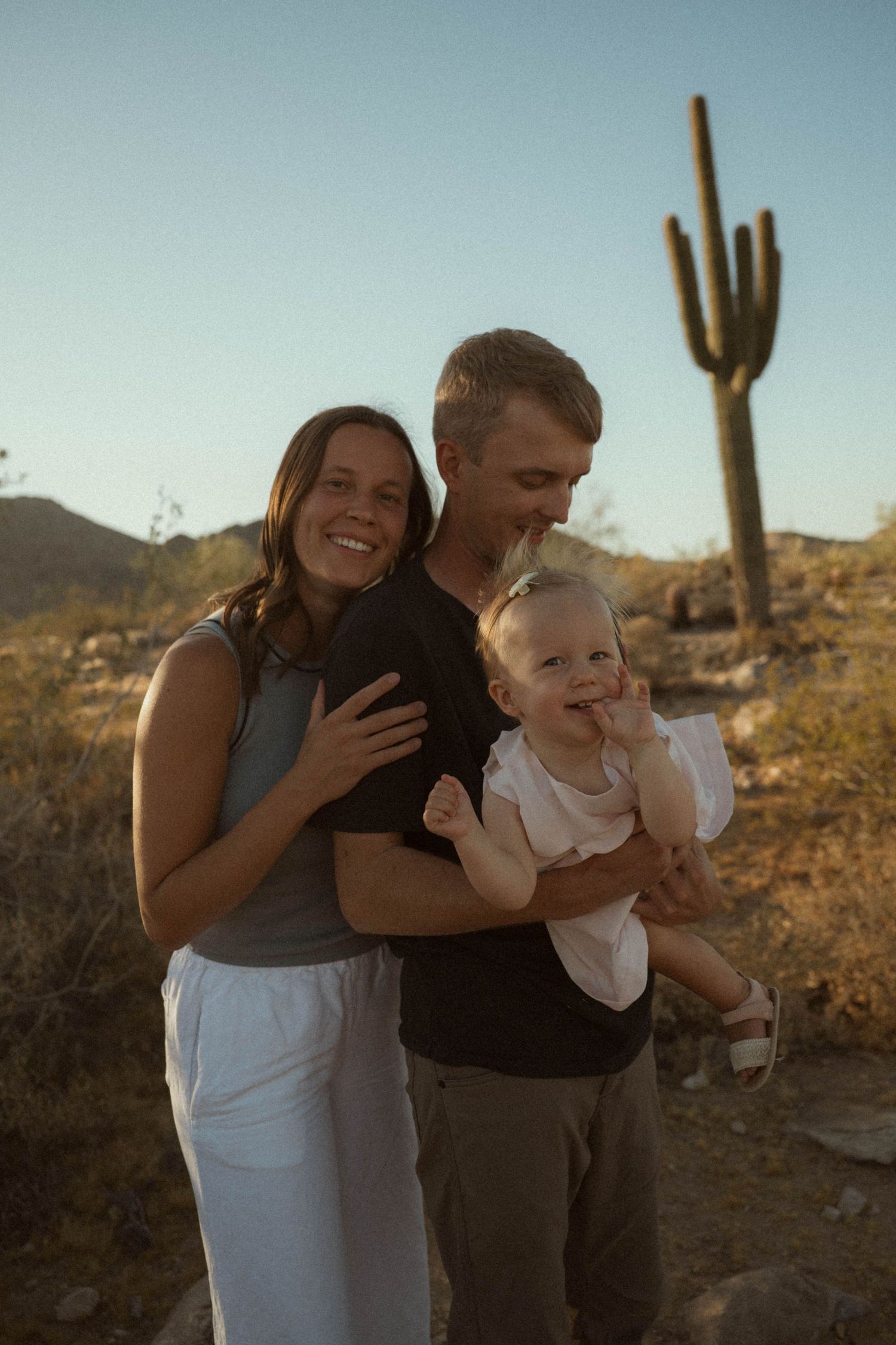 A smiling family of three poses in the Arizona desert with a saguaro cactus at golden hour.