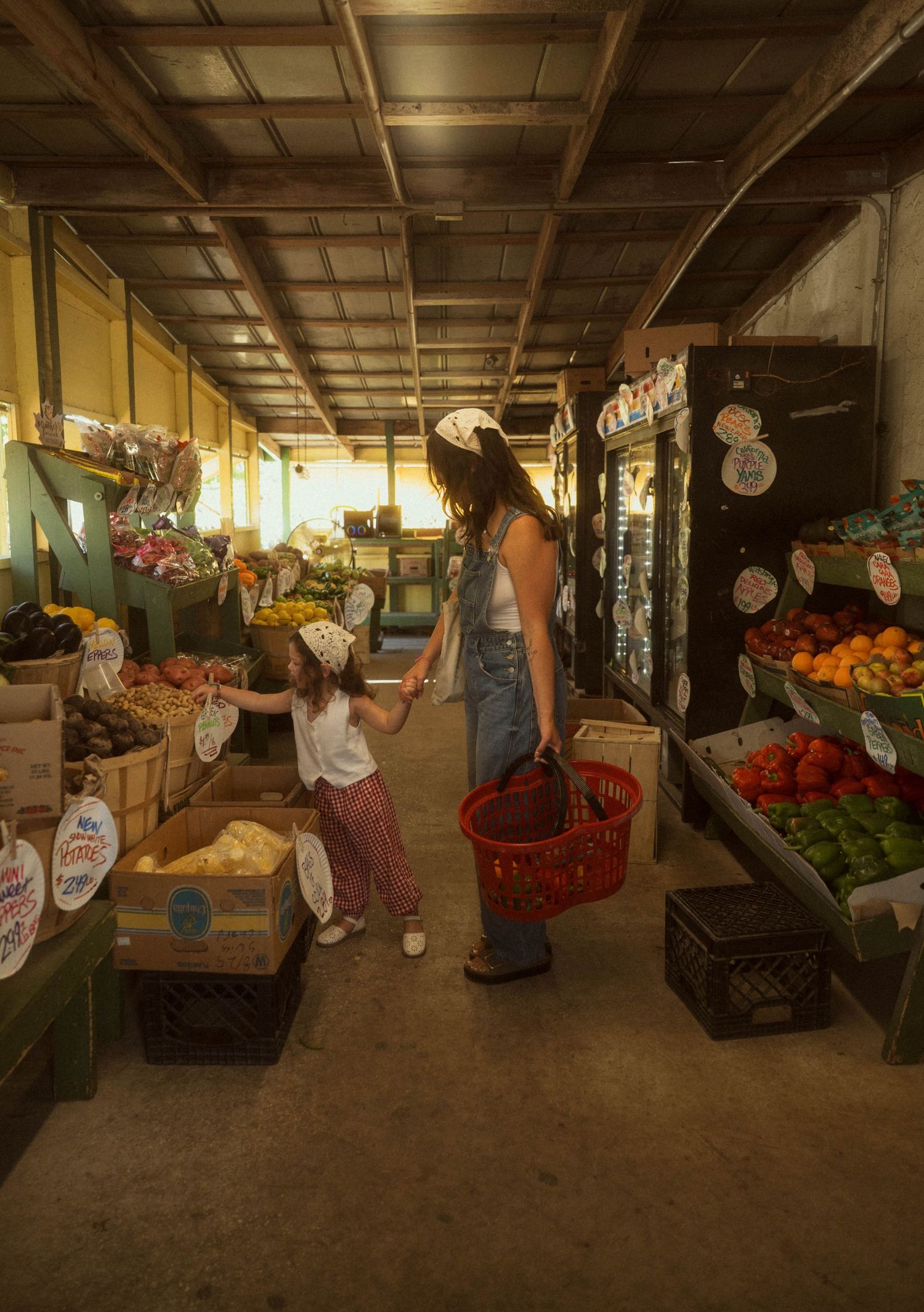 A mother and child shop for fresh produce at a vibrant farmers market, holding hands while browsing colorful fruits and vegetables.