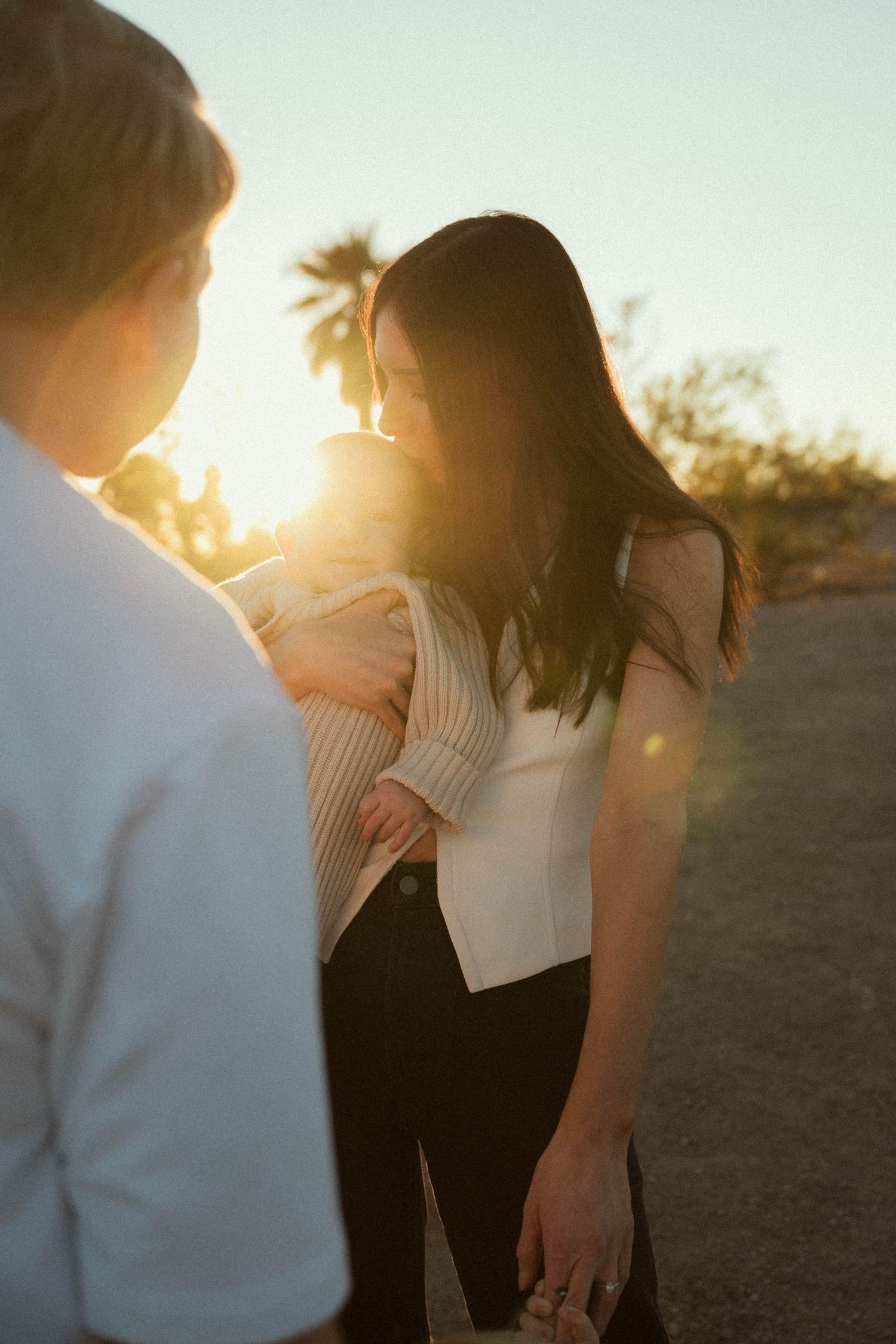 A couple shares an intimate moment during golden hour sunset in a desert landscape, with soft backlighting creating silhouettes.