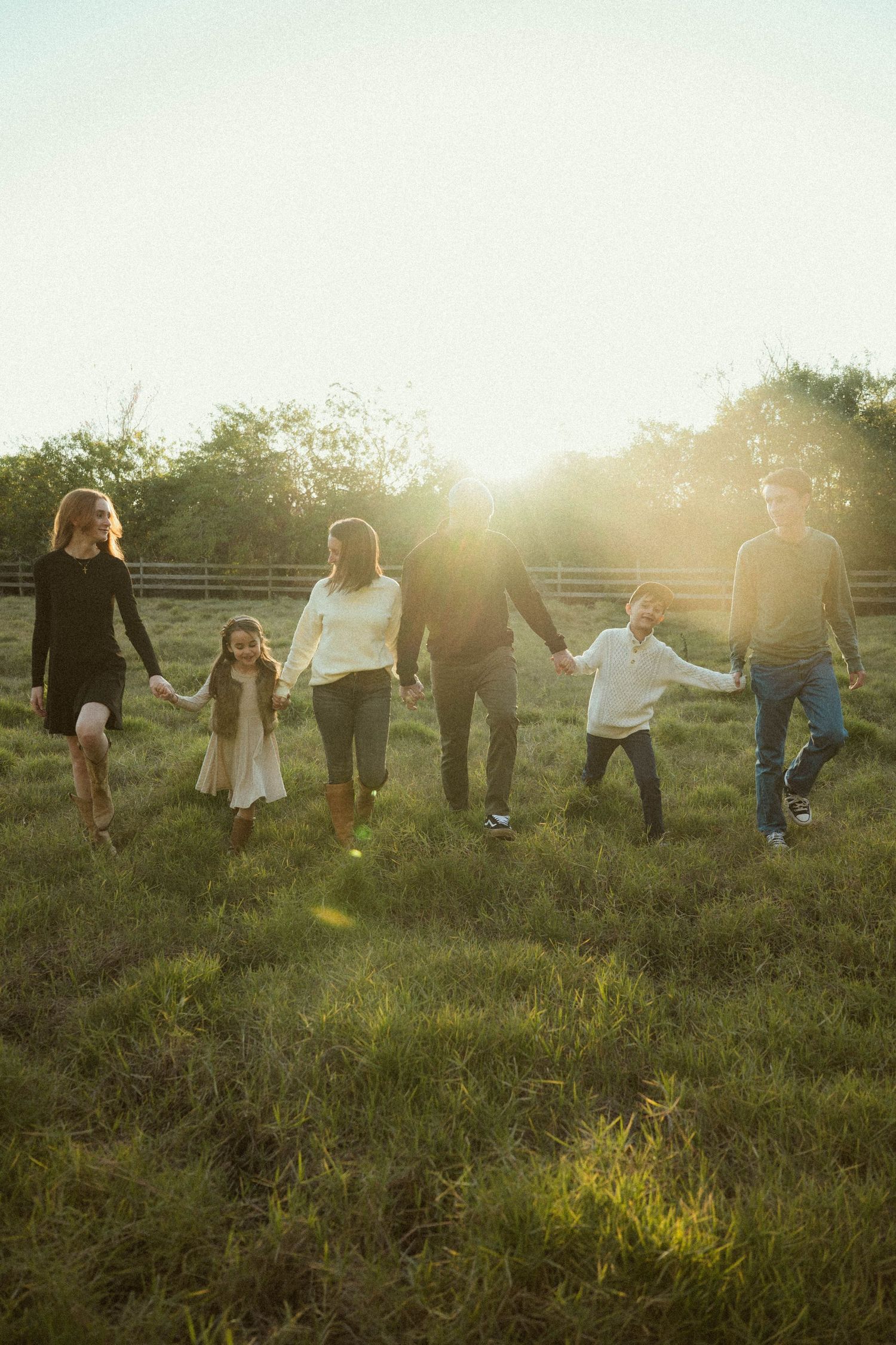 A group of people holding hands while walking across a sunlit grassy hillside at golden hour.
