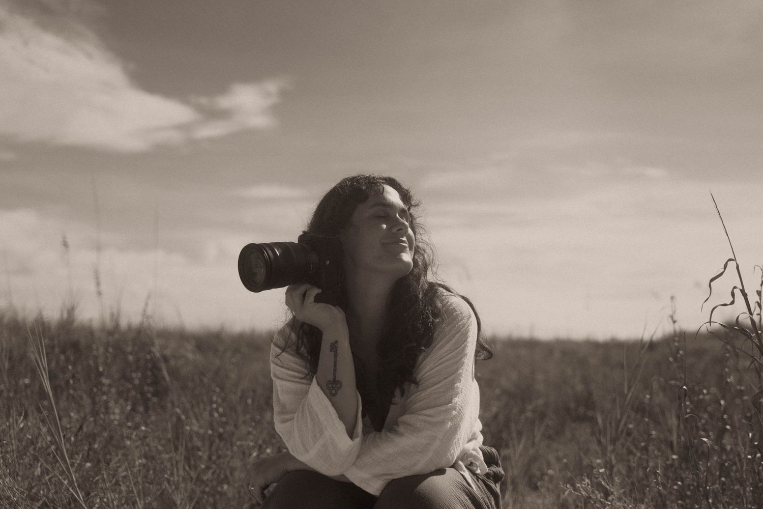 Woman photographer capturing shots outdoors in a field, holding camera, sepia-toned artistic photo.