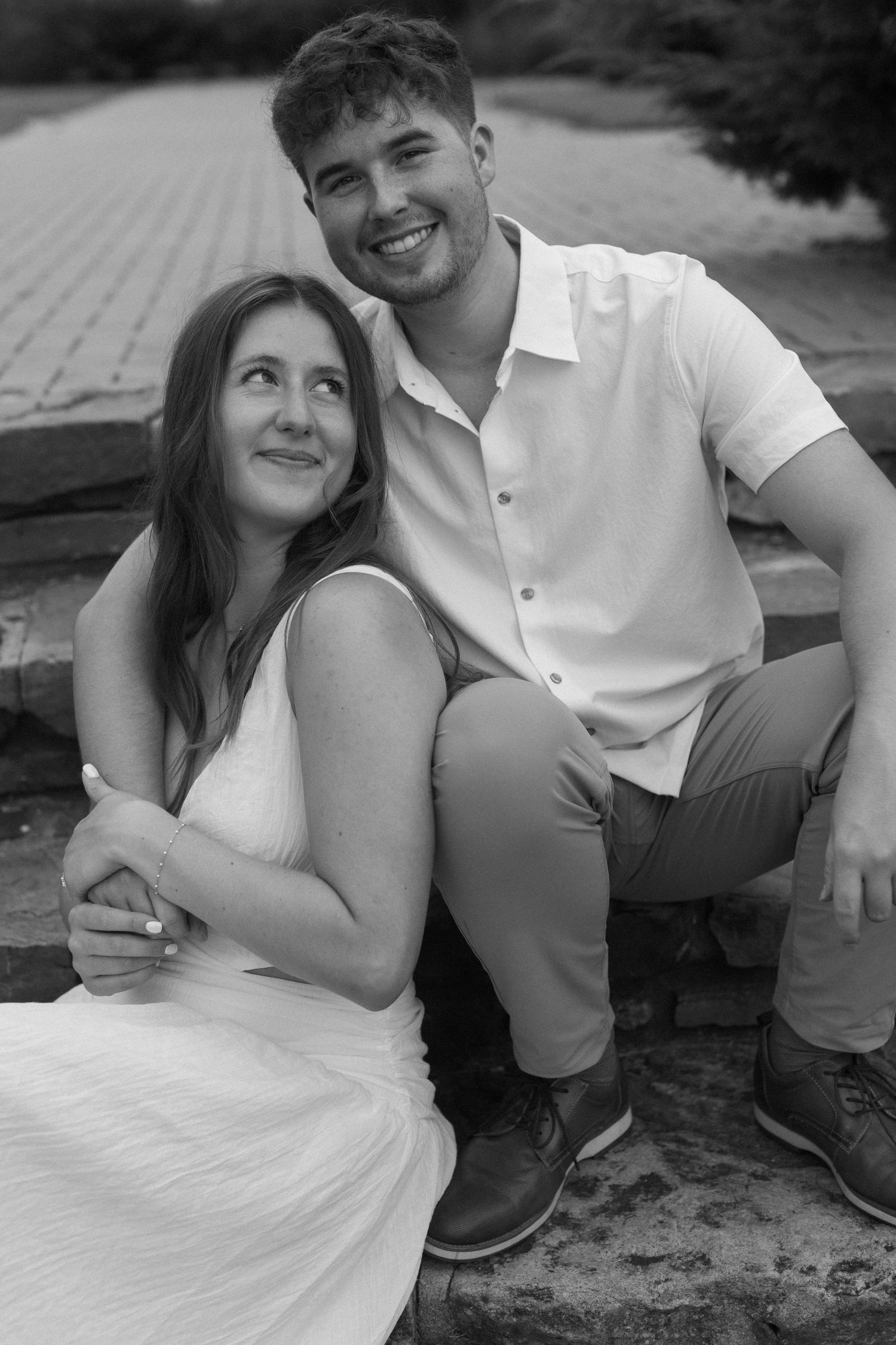 A black and white portrait of a couple sitting together outdoors sharing a tender moment.