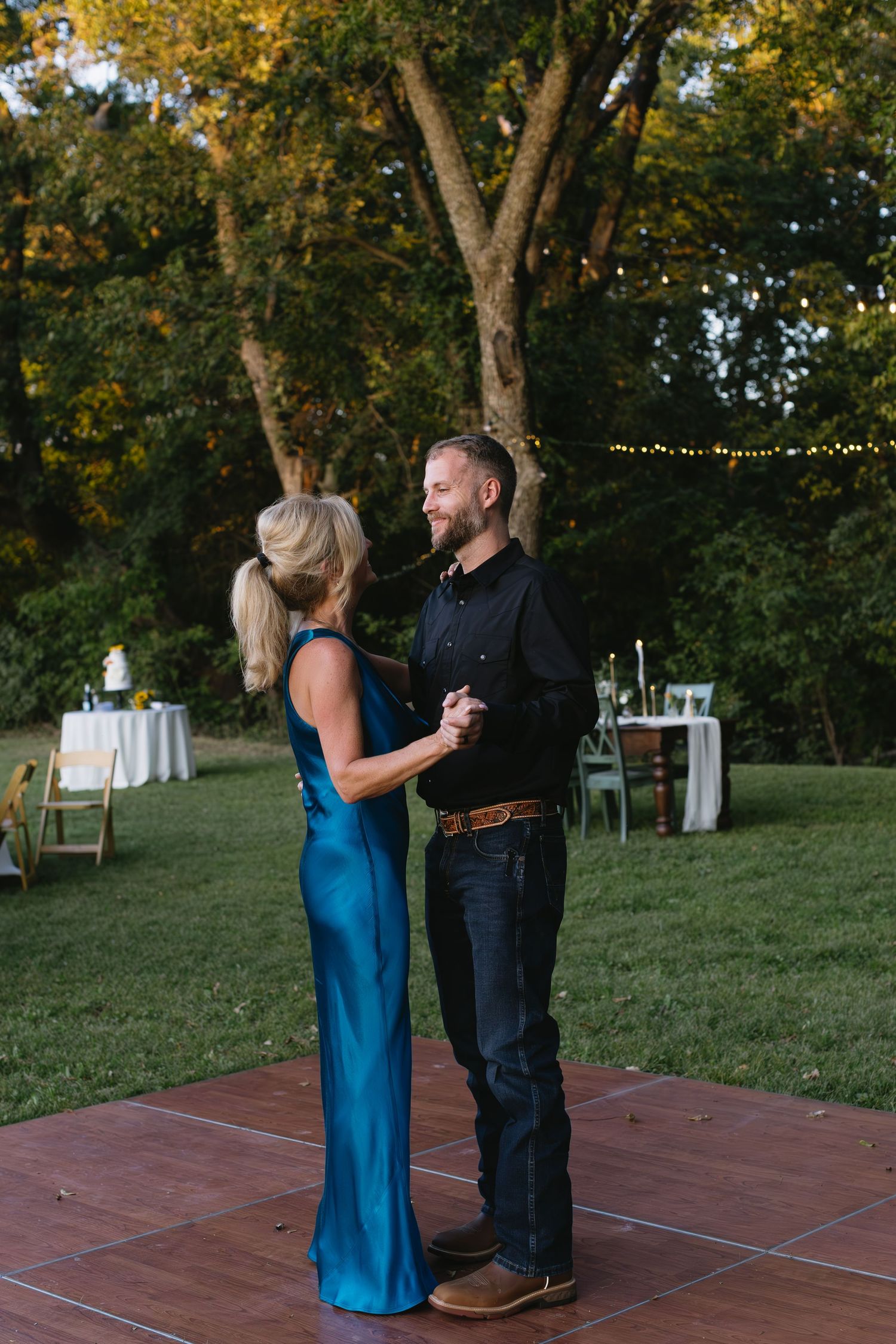 Couple dancing on a wooden platform outdoors during sunset.