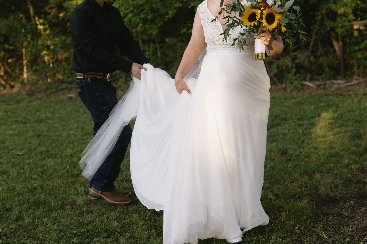 Bride holding vibrant sunflower bouquet in flowing white gown outdoors.