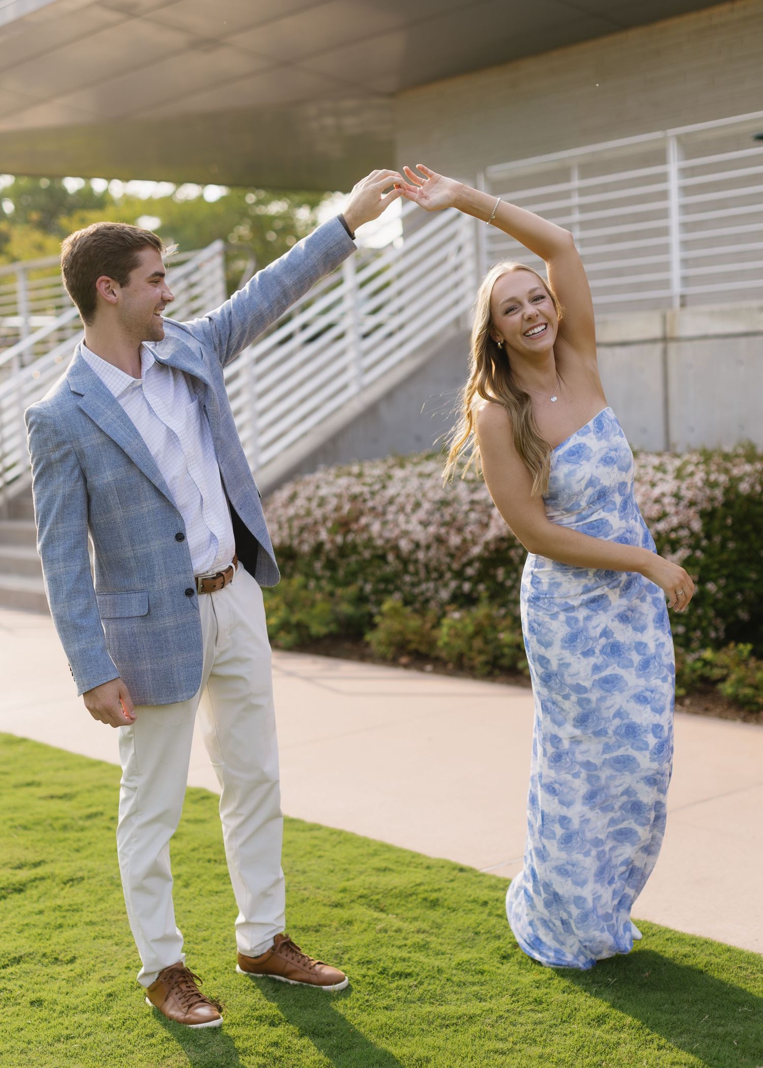 A couple in blue and white outfits dances and twirls on a sunny outdoor pathway.