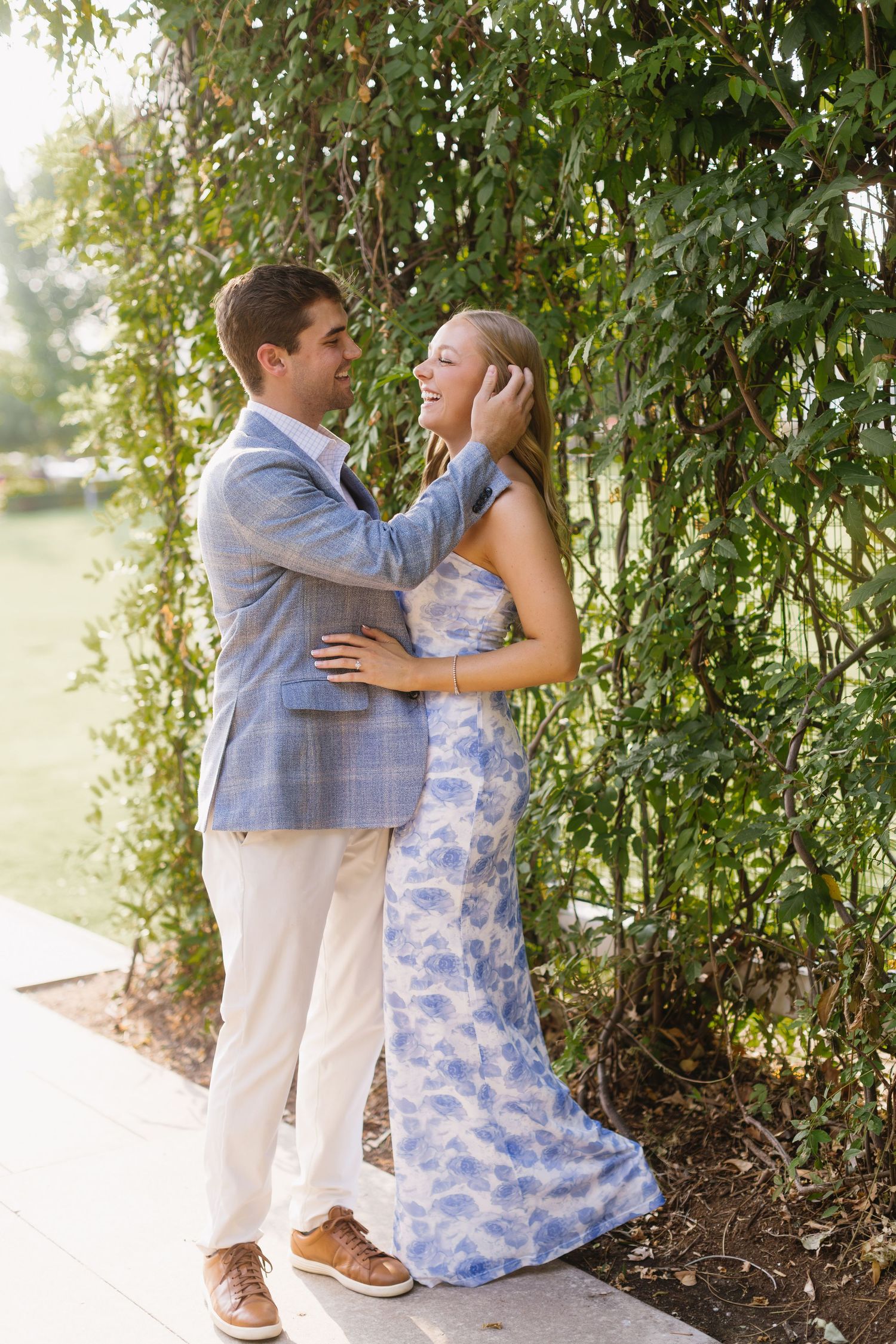 A tender moment captured between a couple embracing on a garden path with hanging willow branches.