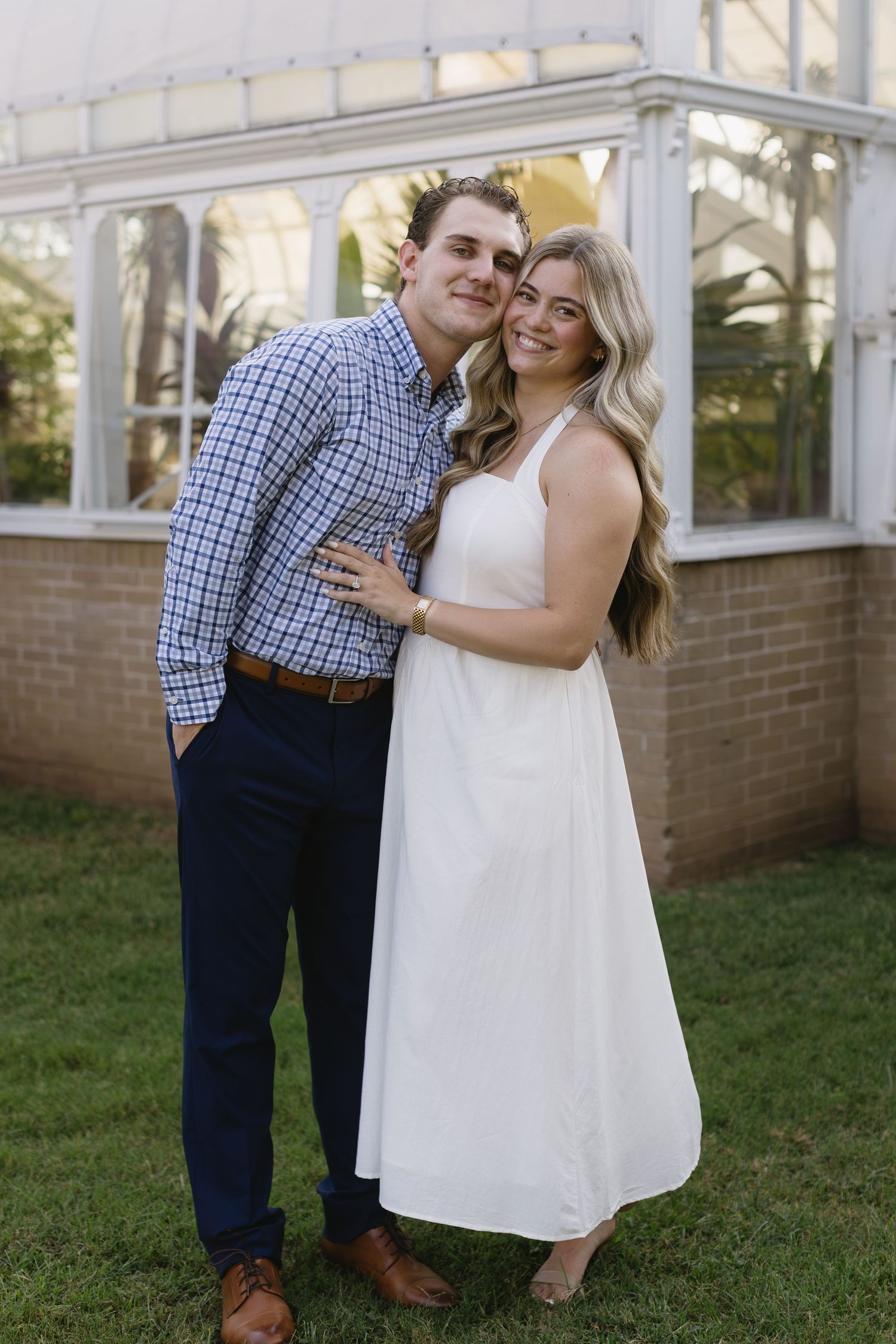 Couple sharing a romantic moment in an outdoor garden setting with a white greenhouse structure visible.