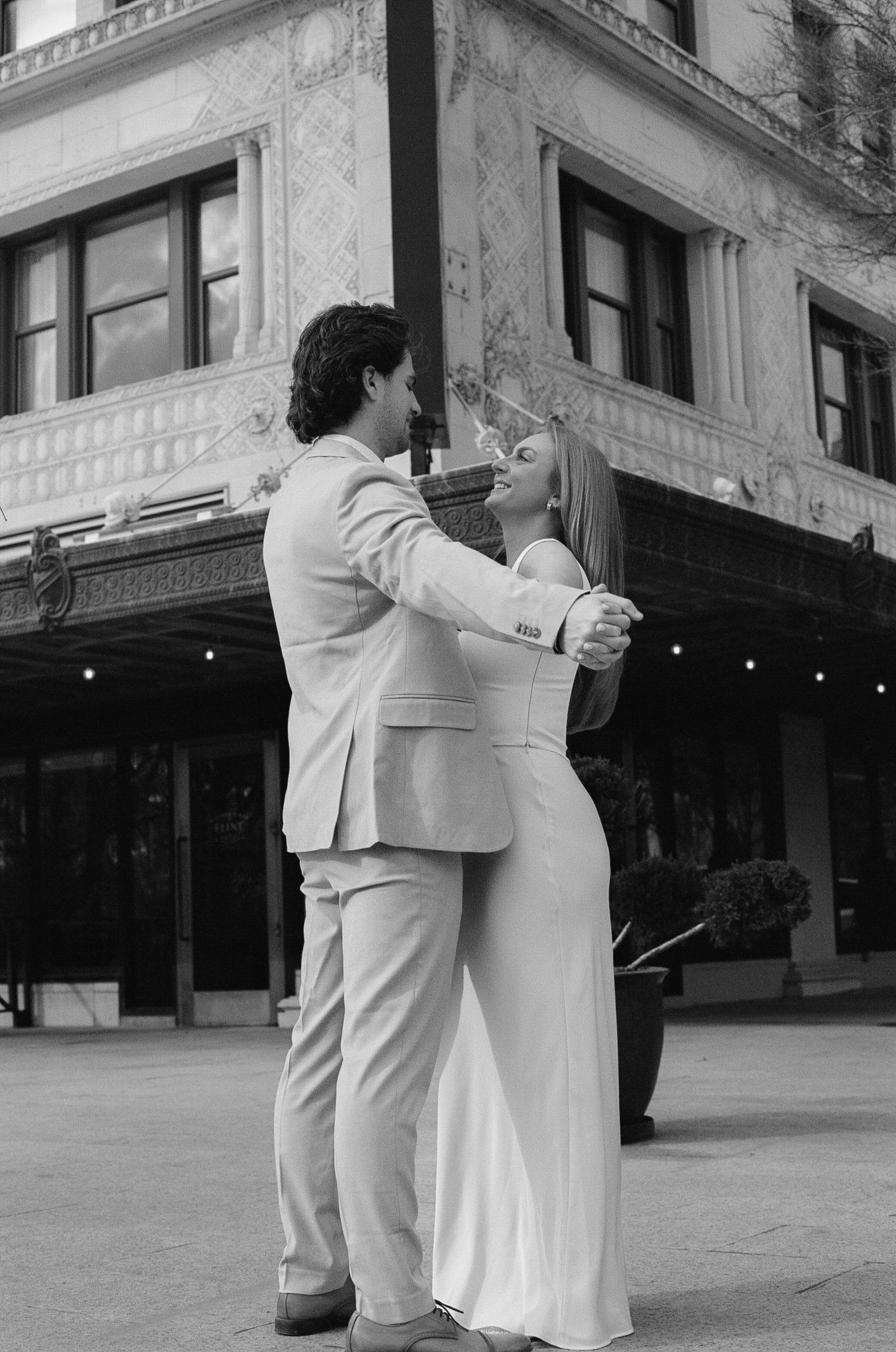 Black and white photo series of a couple dancing together in formal wear outside a building.
