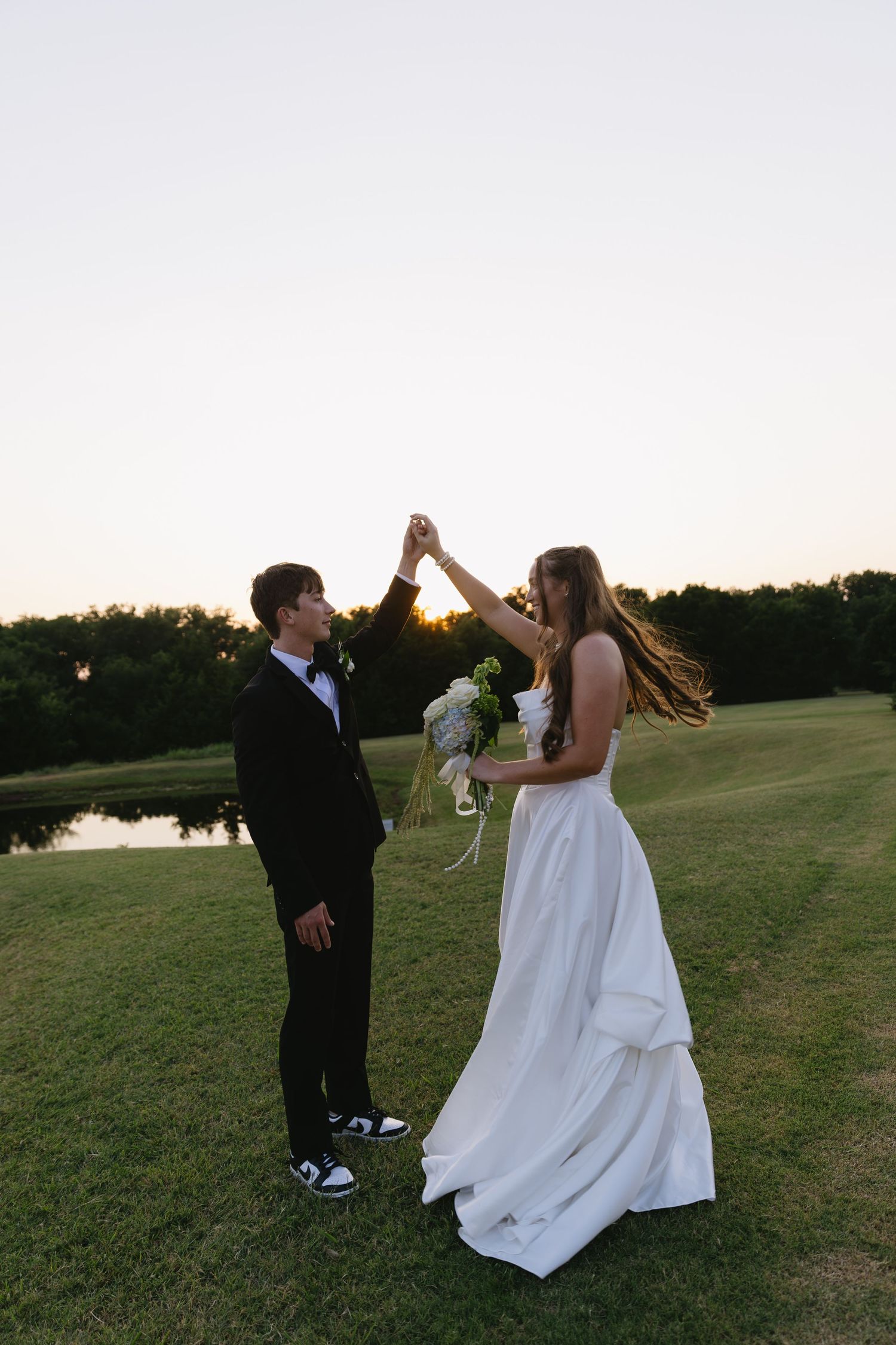 Wedding couple dancing and twirling on a grassy hill at golden hour.