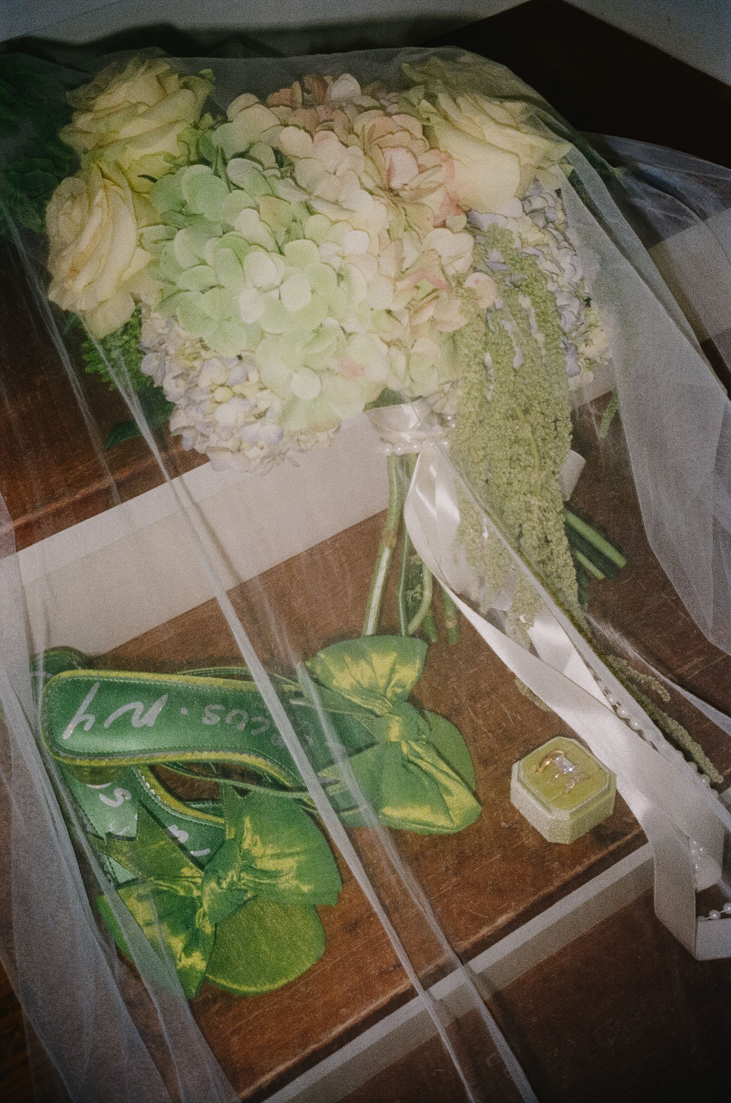 White hydrangea and rose wedding bouquet with green ribbon and heels on wooden surface.