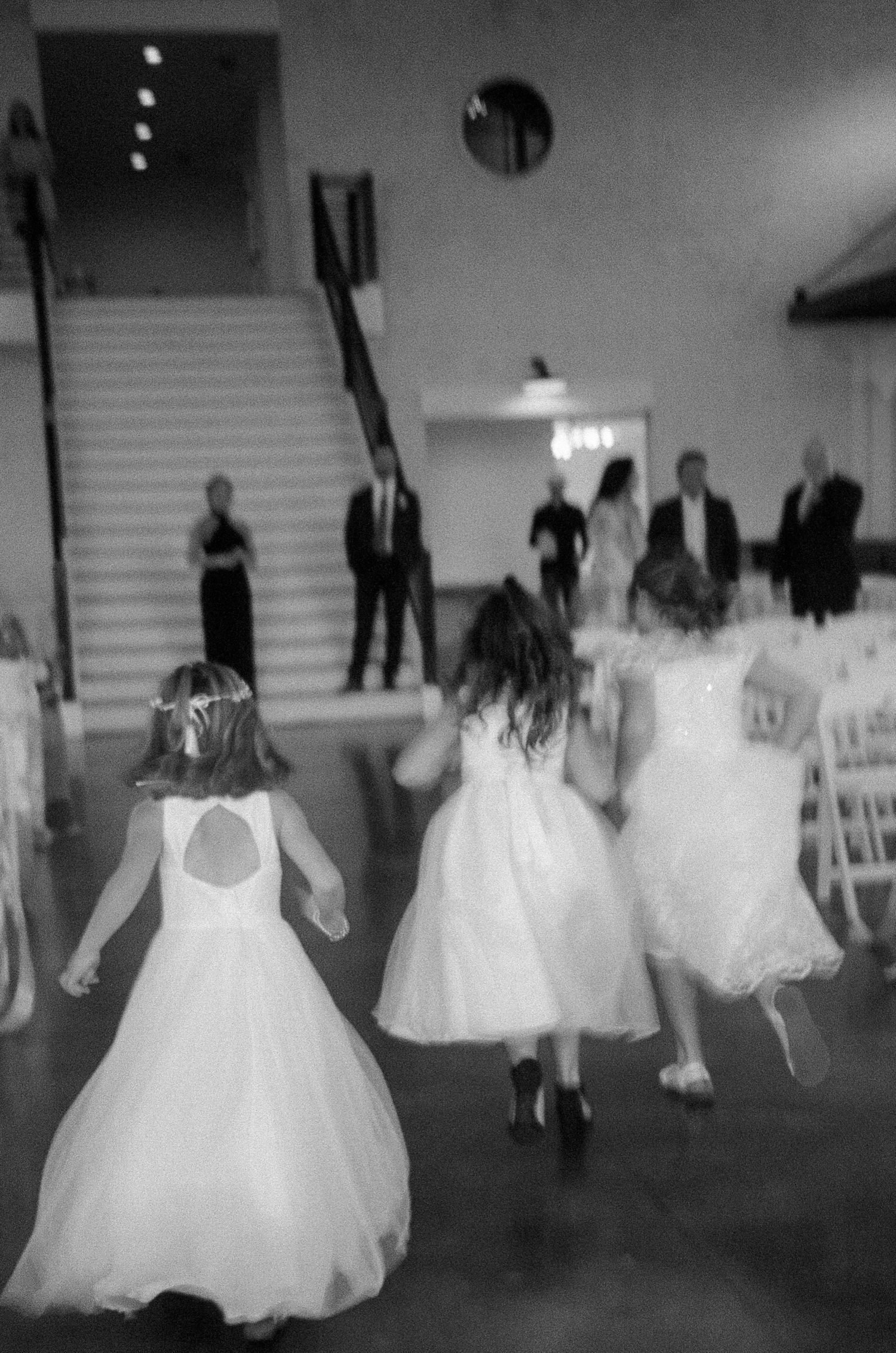 Motion-blurred black and white photo of people dancing in formal white dresses at an event.
