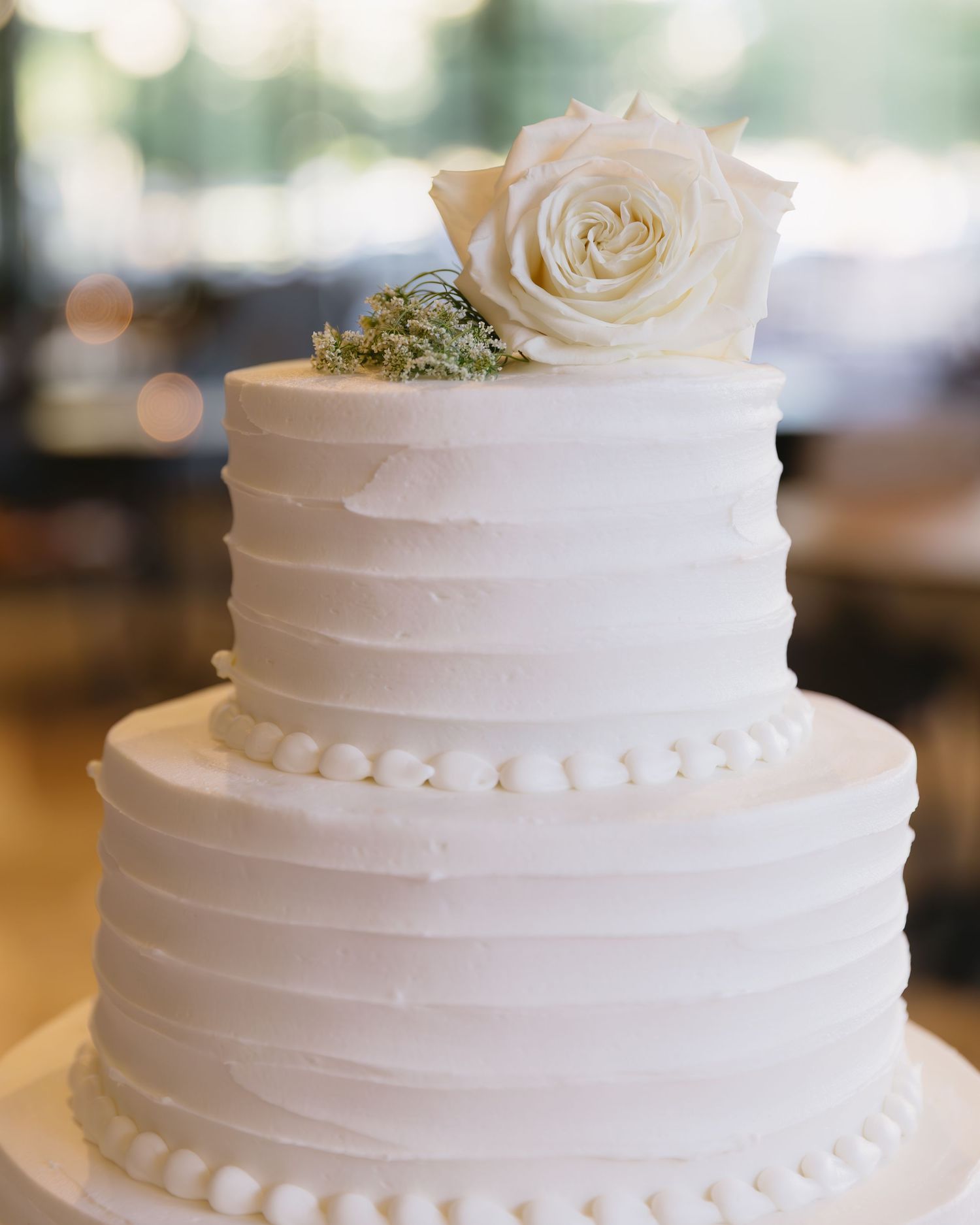 Elegant white wedding cake with simple horizontal ribbed texture and delicate pearl accents.