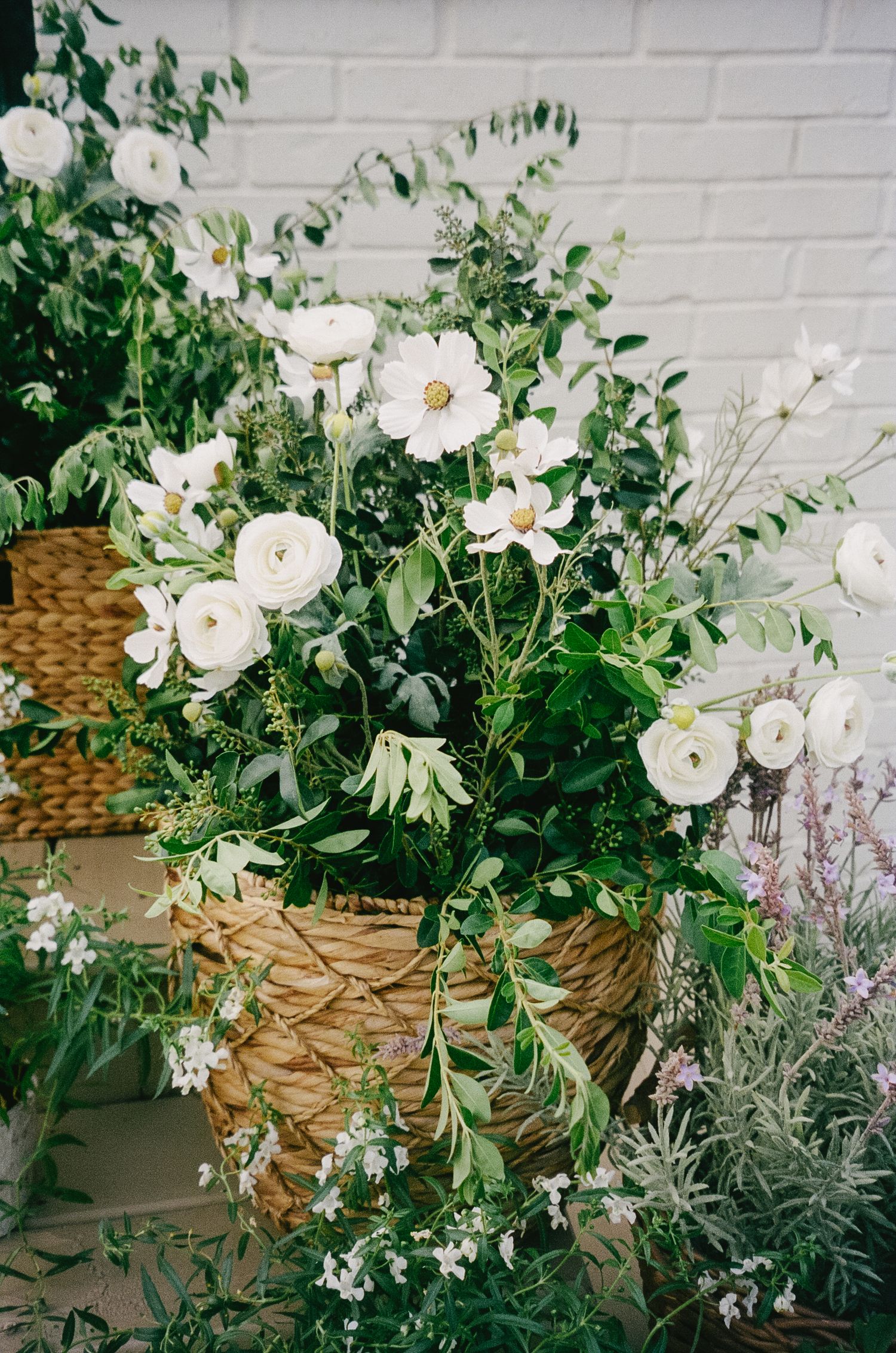 A lush arrangement of white flowers and greenery in a woven basket.