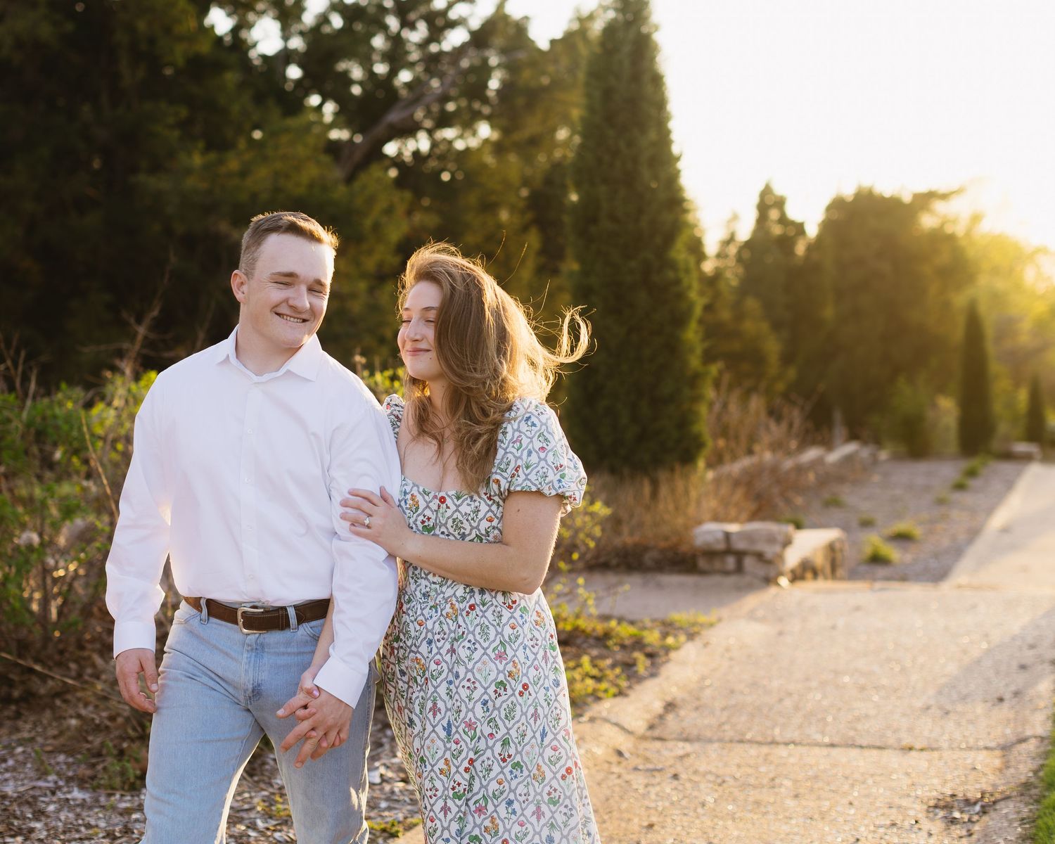A couple walks together on a path during golden hour with sunlight streaming through trees.