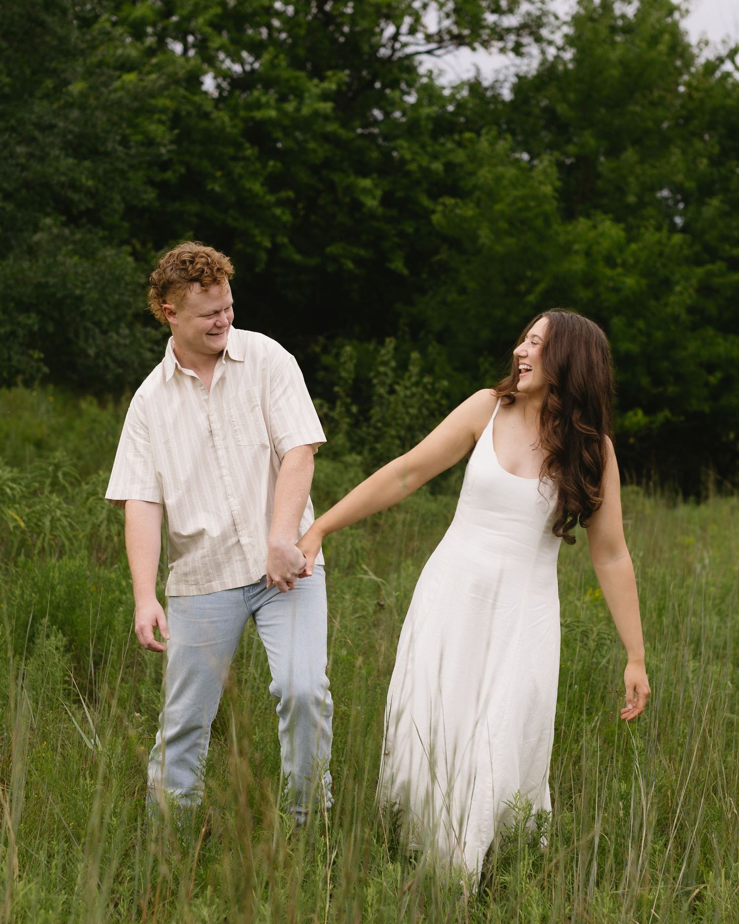 A couple walks hand in hand through a grassy meadow in a romantic photoshoot sequence.