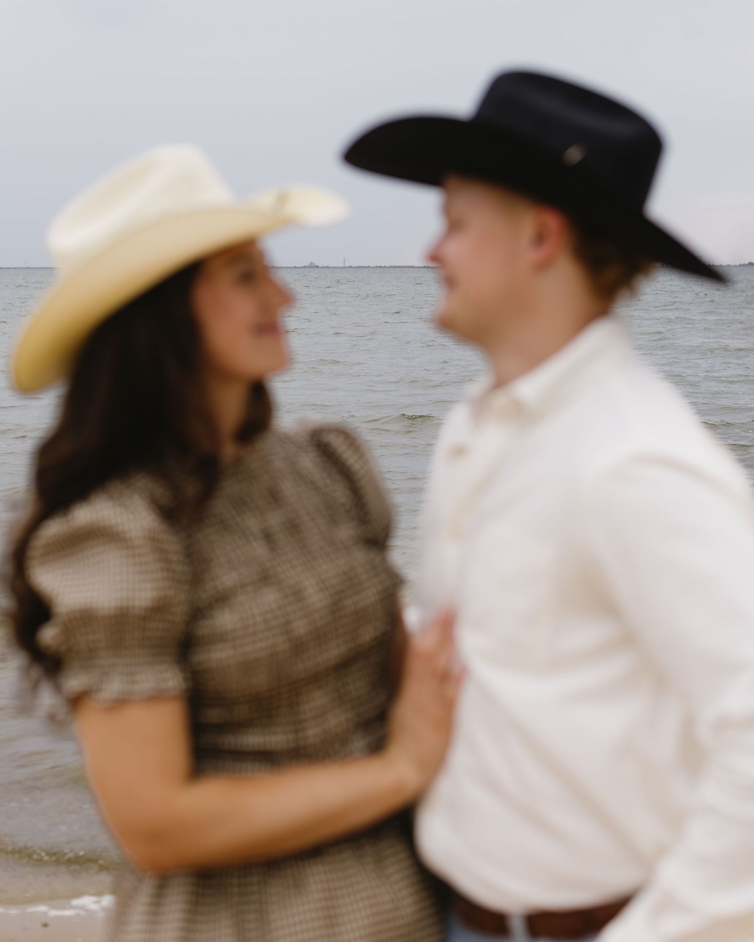 Two people wearing cowboy hats share an intimate moment by the waterfront.