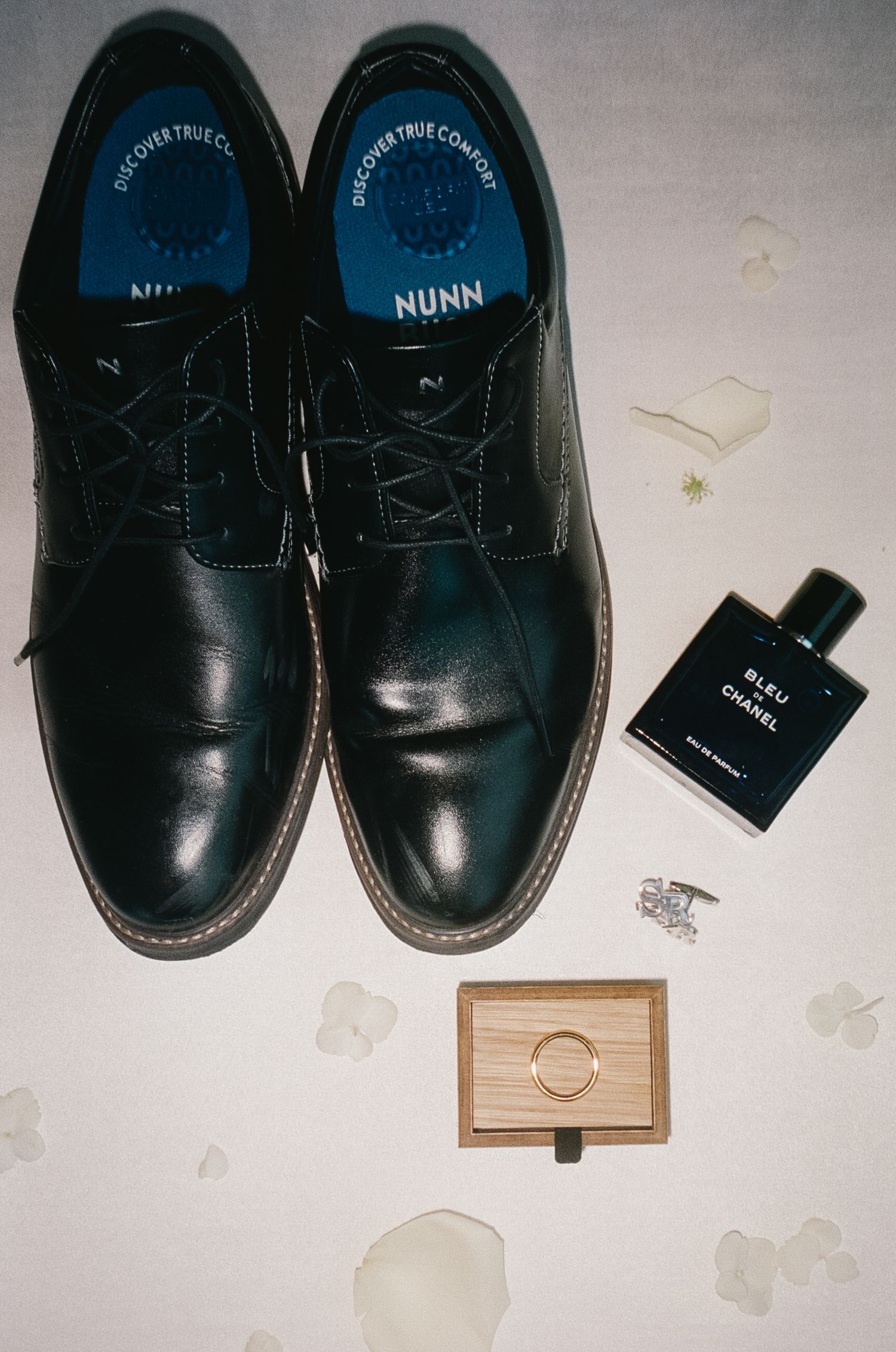 A black leather dress shoe sits next to a small glass bottle and wooden box on a white surface.
