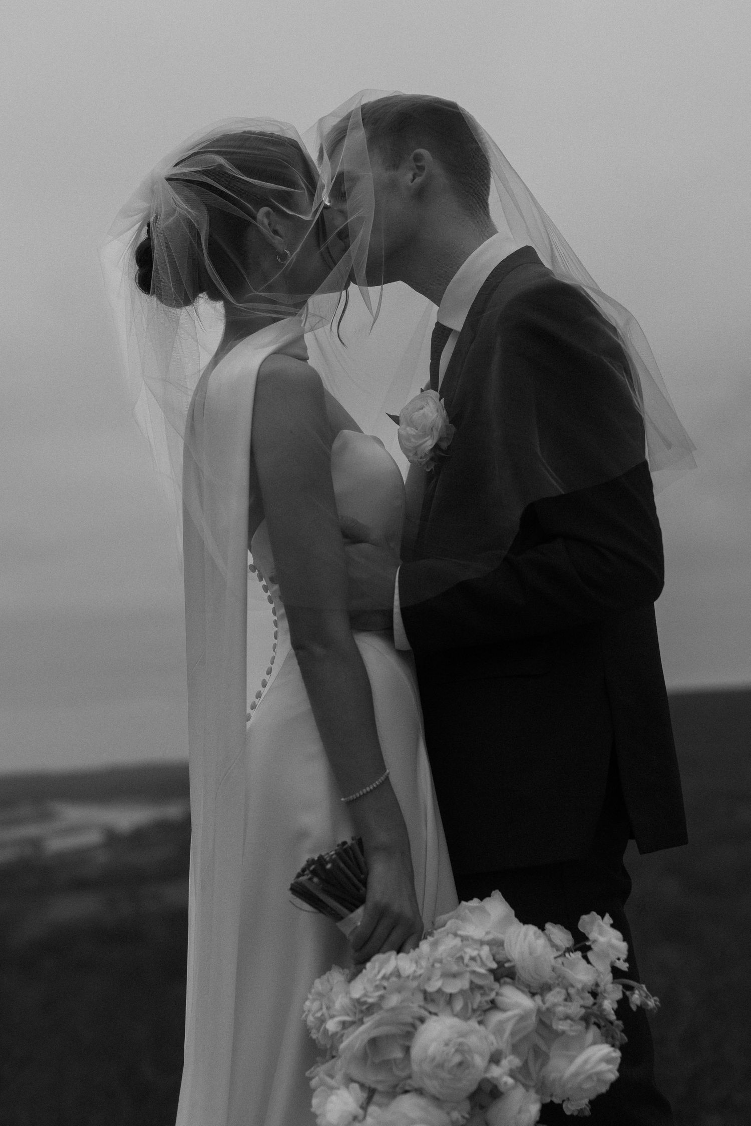 Black and white portrait of newlyweds sharing an intimate moment with white bouquet.