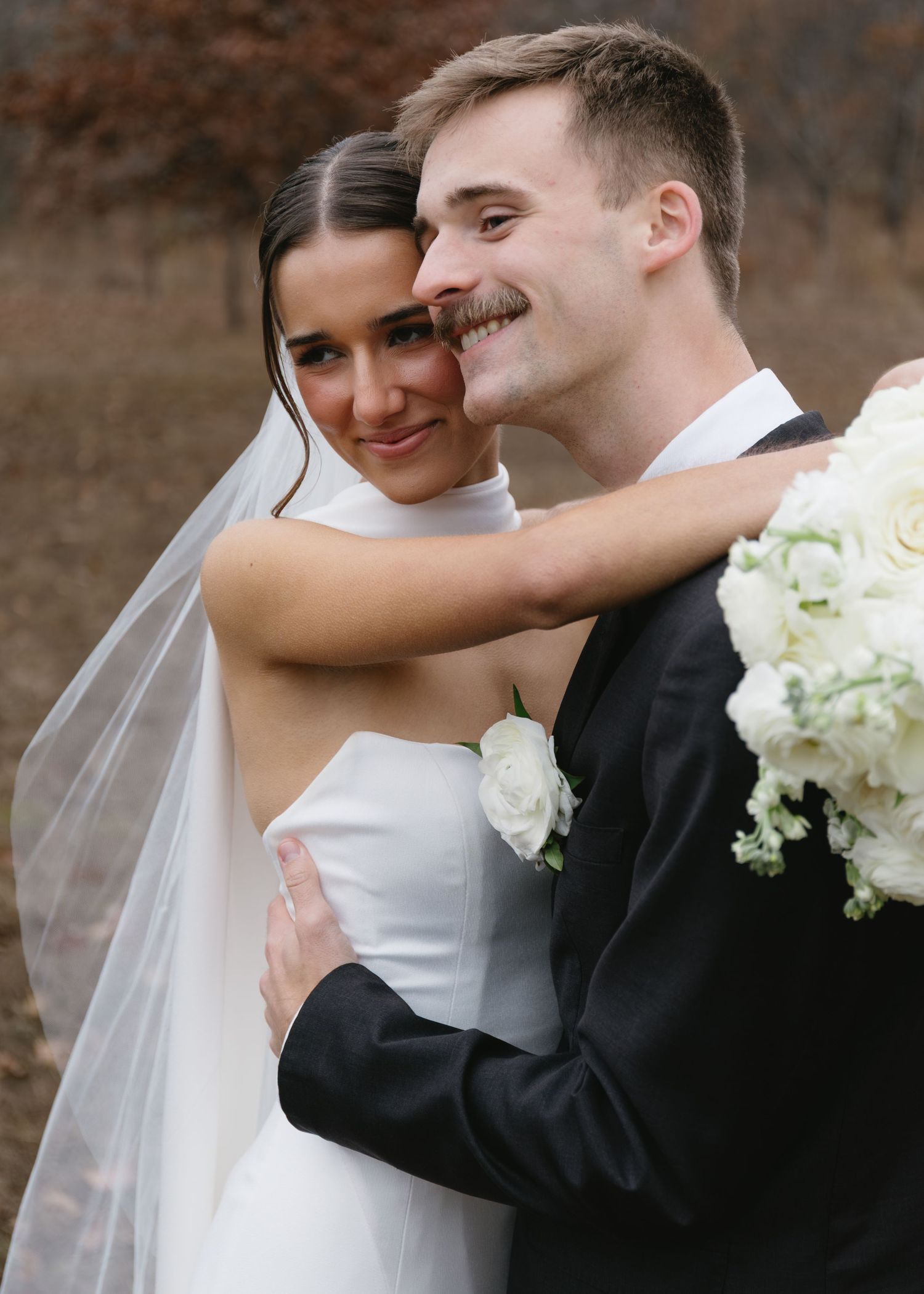 Intimate wedding couple moment captured against rustic brick wall with white bouquet.