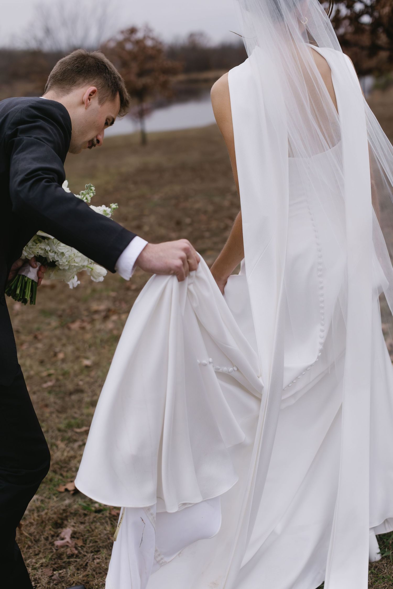 Close-up details of flowing white wedding dress and veil against natural outdoor backdrop.