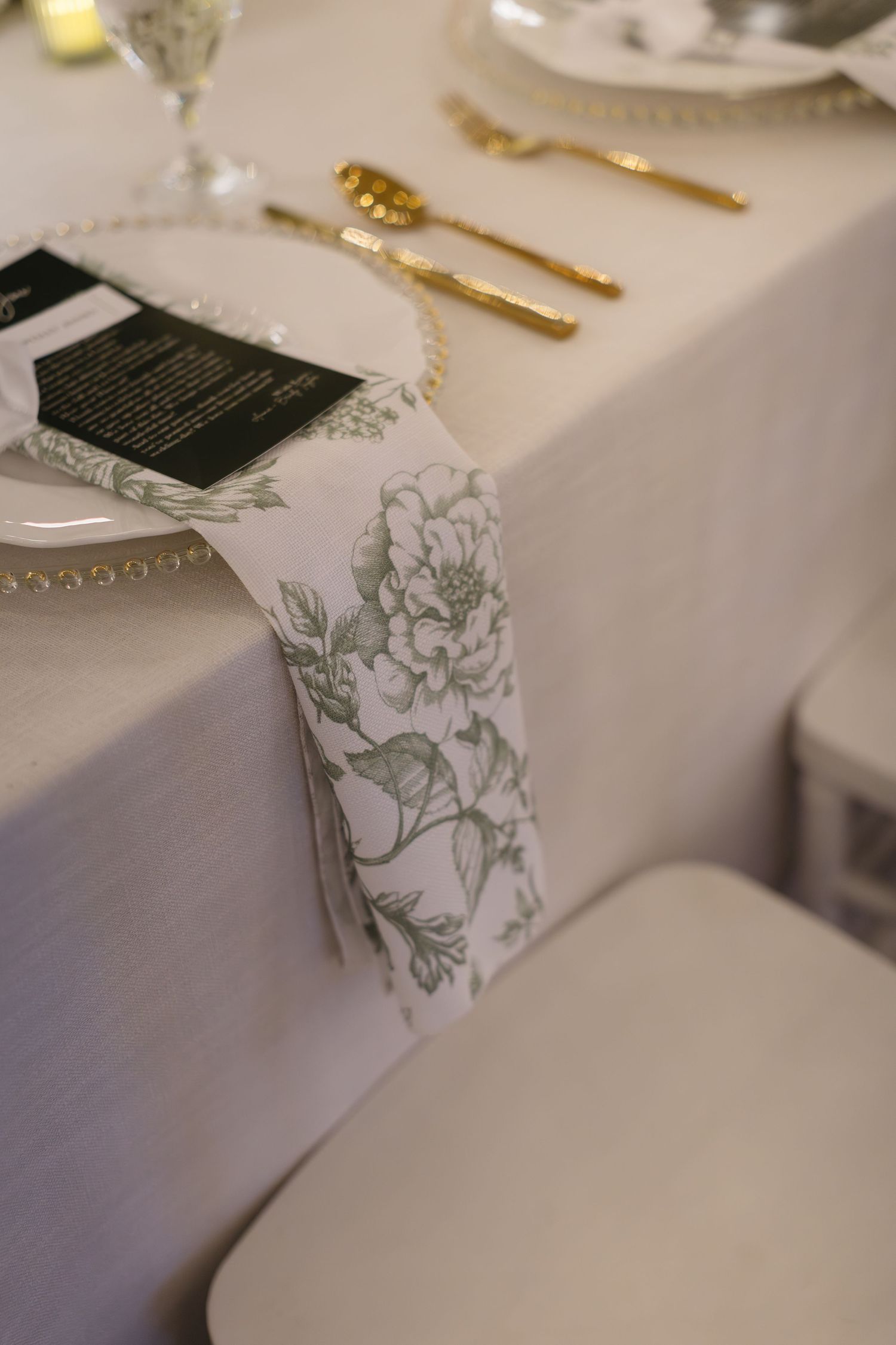 Elegant wedding table settings with floral patterned votive holders and gold cutlery on white linens.