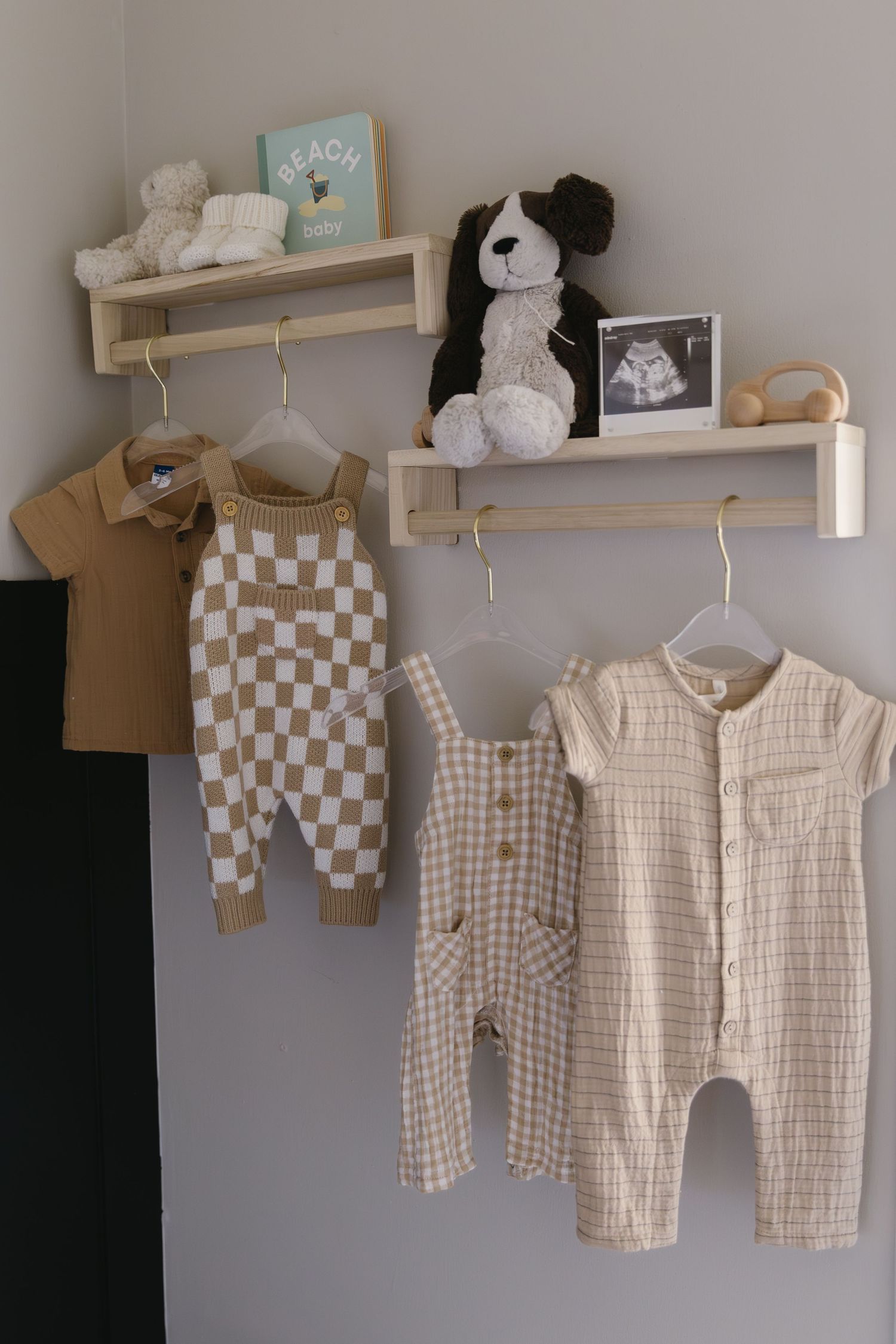 Neutral baby clothes and stuffed animals displayed on wooden wall shelves in a nursery.
