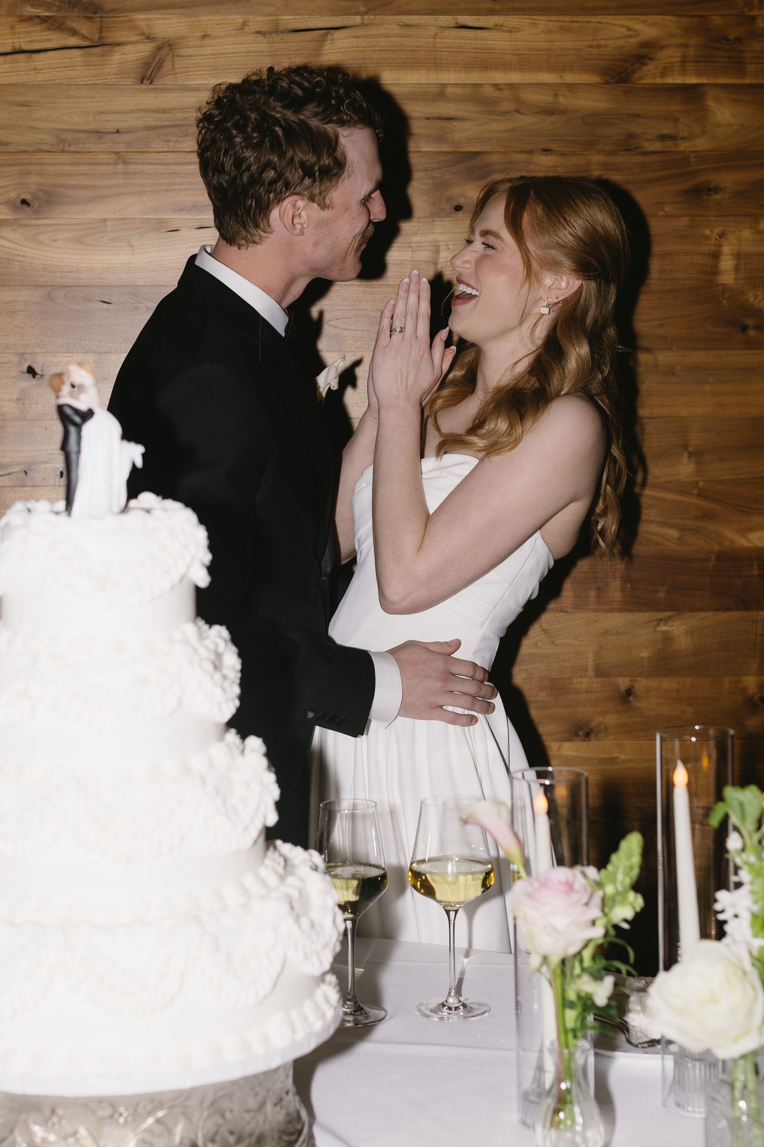 Romantic moment between newlyweds at their reception with elegant white wedding cake.