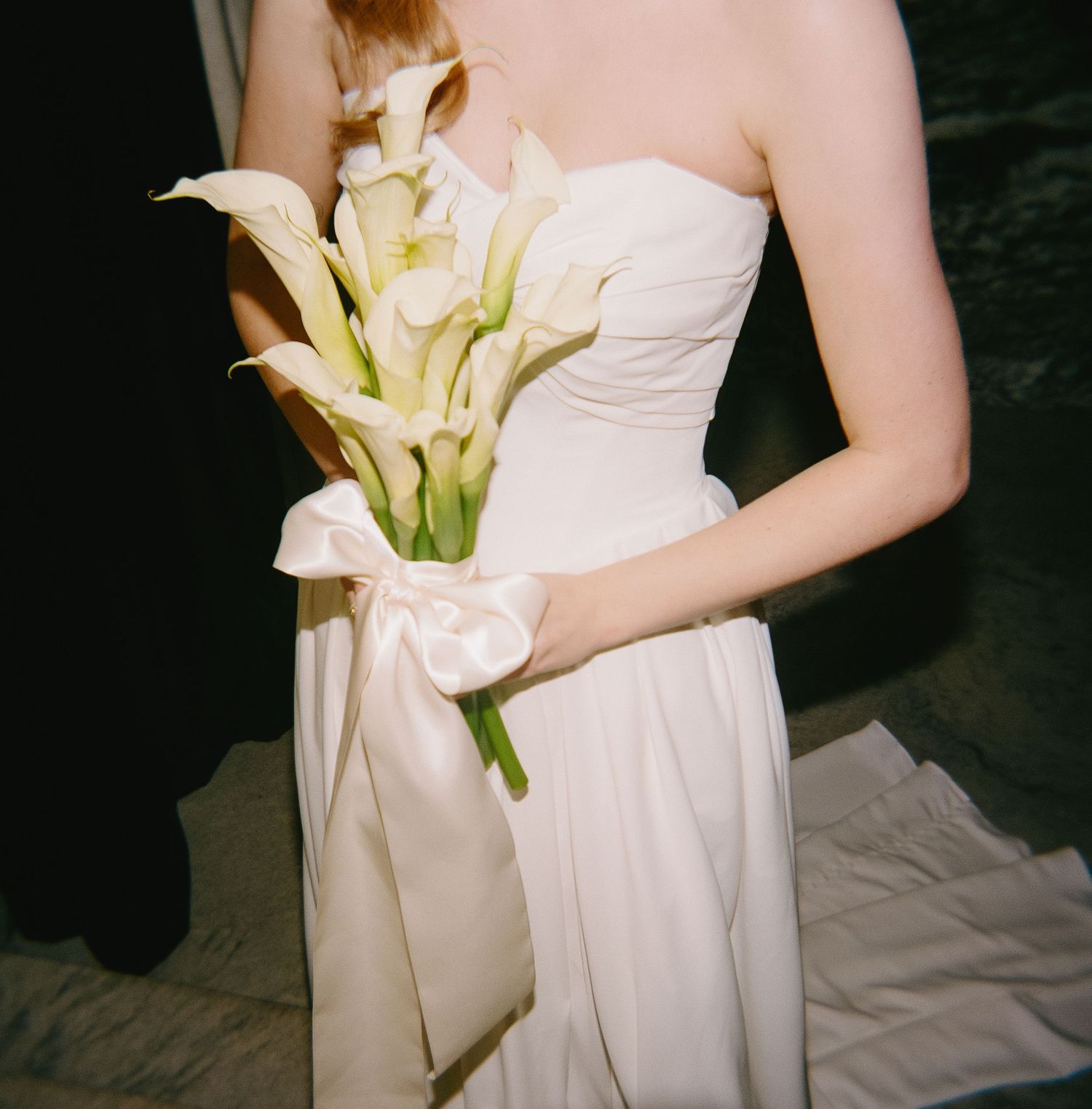 Elegant calla lily bouquet held against white wedding gown.
