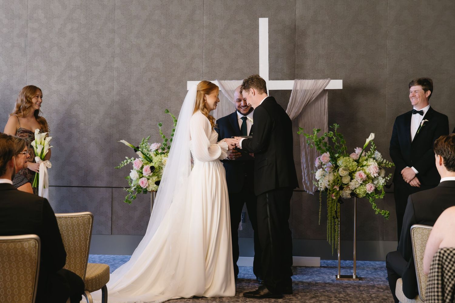Elegant wedding reception setup with guests in formal attire against grey walls.