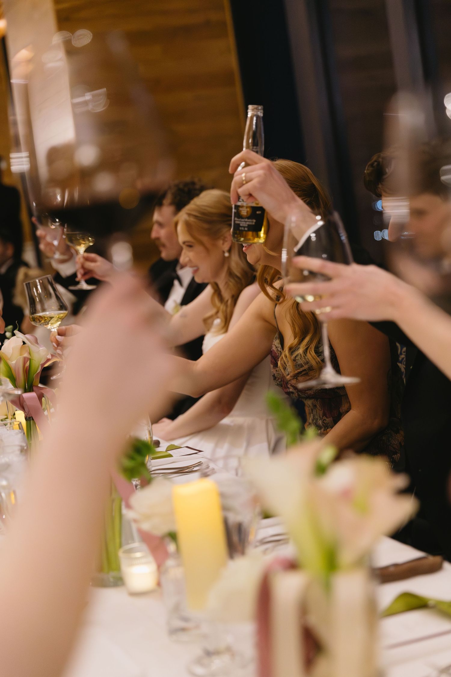 Wedding reception guests raising glasses in a toast at an elegant dinner table.