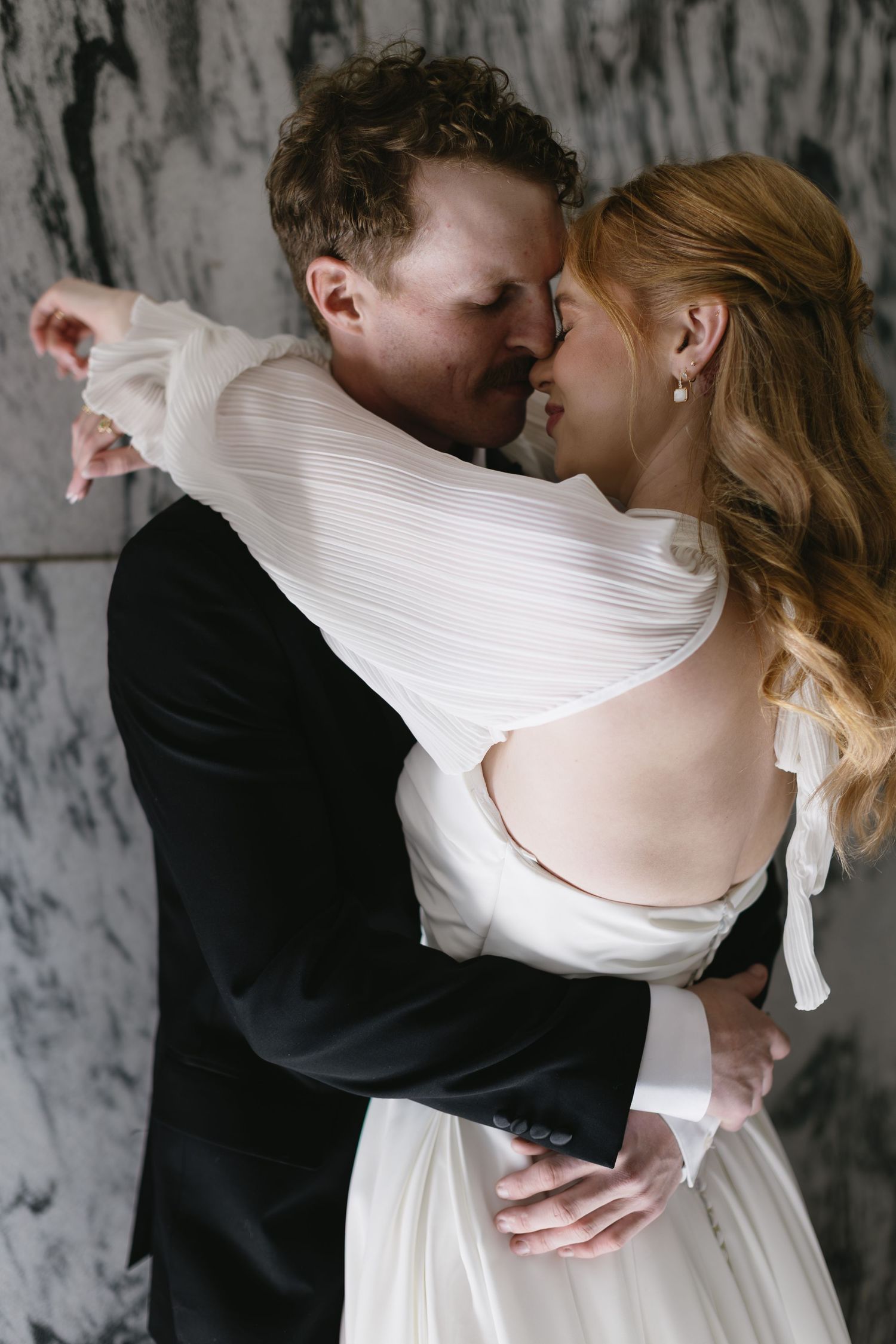 Romantic wedding couple embracing in intimate poses against a marble wall background.