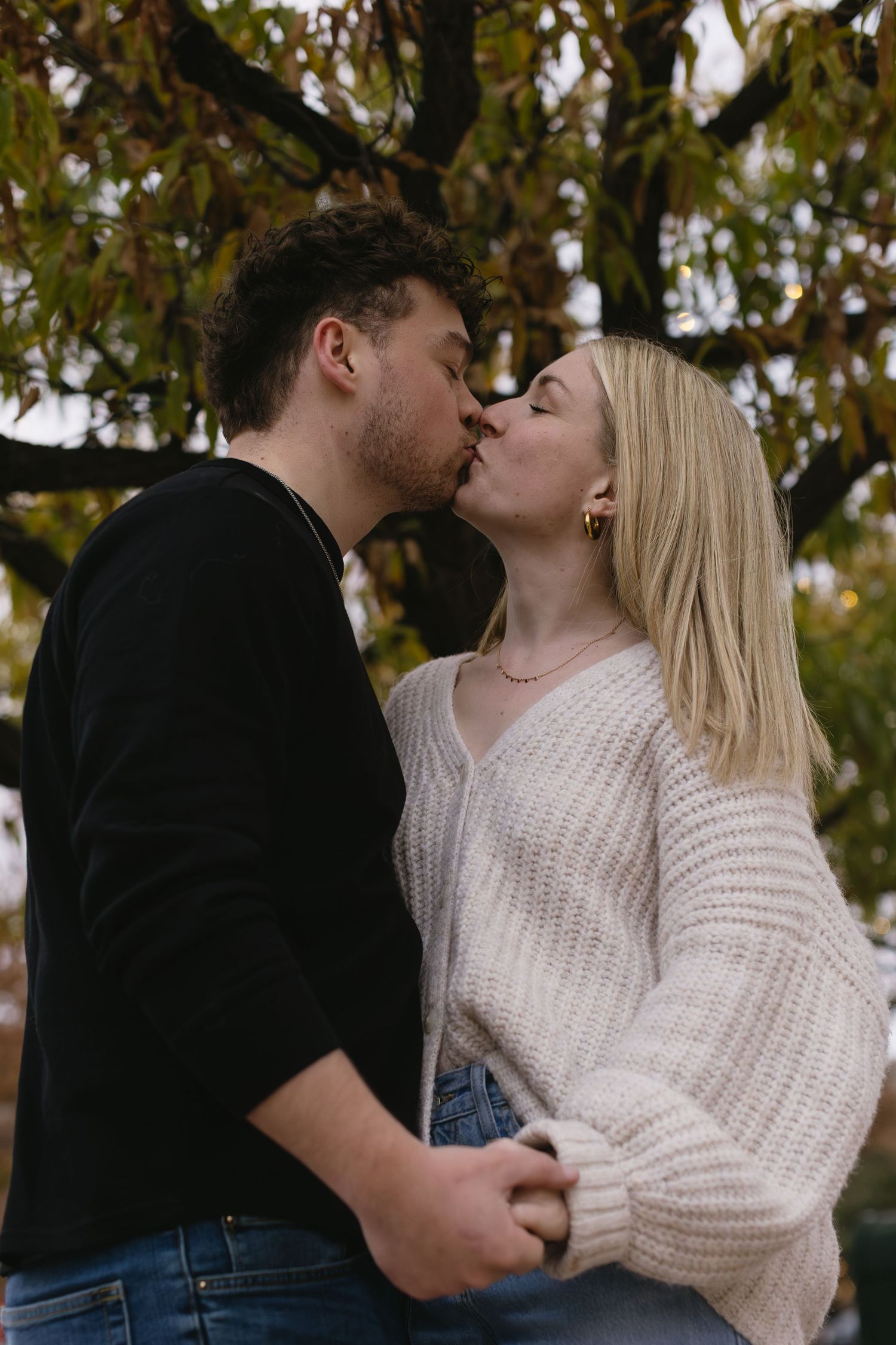 Intimate couple sharing romantic kisses under autumn trees in casual attire.